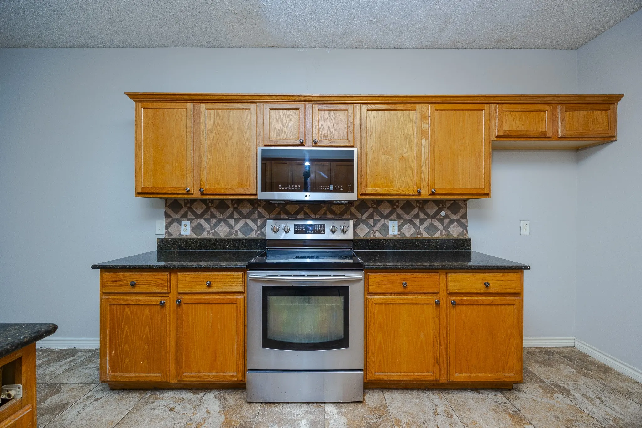 Wood-finish cabinetry, dark speckled countertops, stainless steel range, and built-in microwave