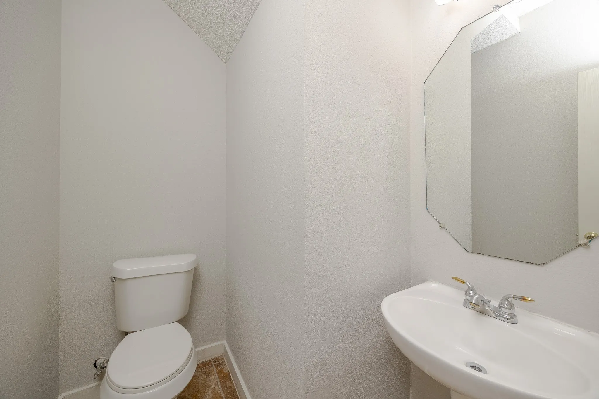 Pedestal sink, wall-mounted mirror, ceramic toilet, and tile flooring