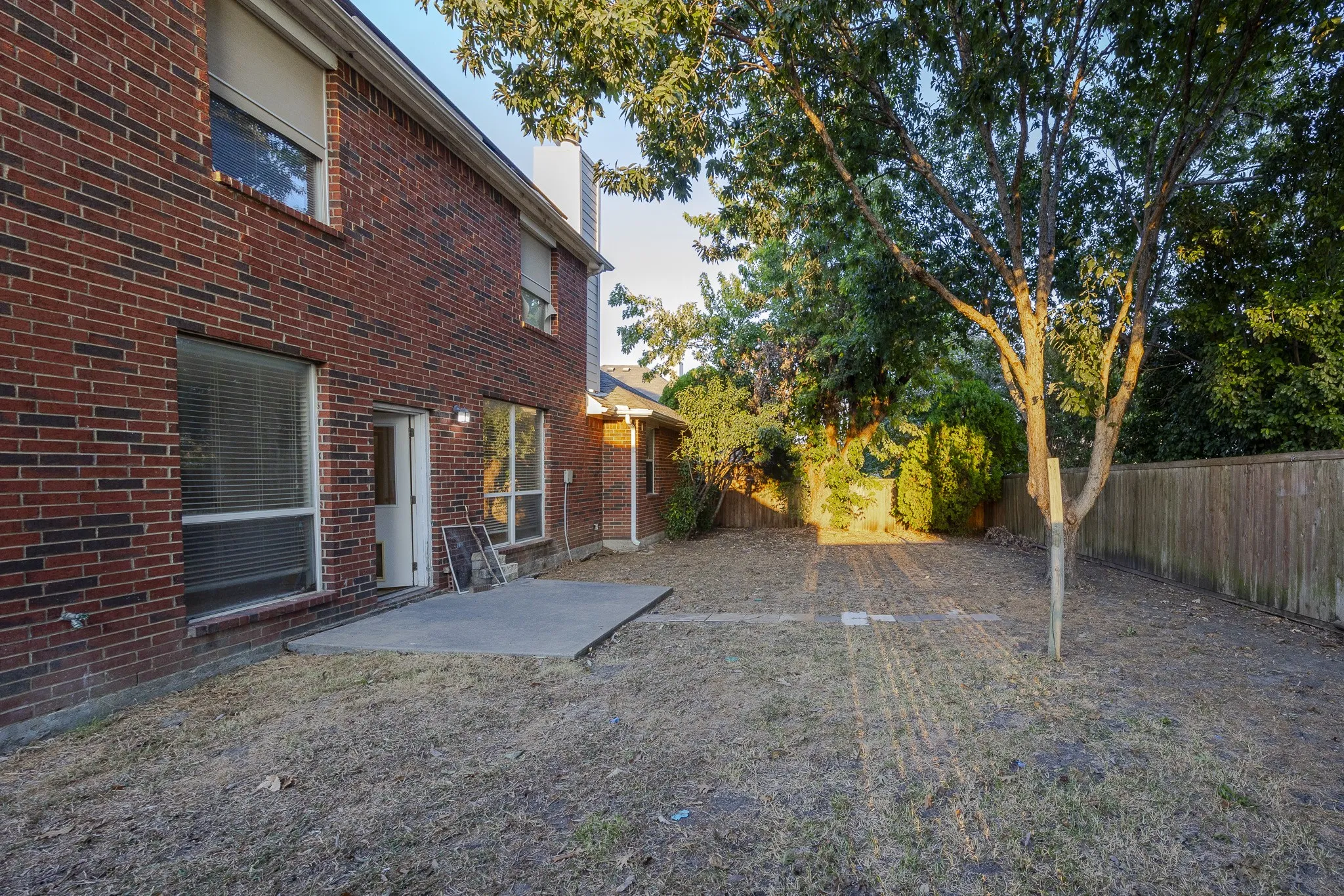 Brick exterior with multiple windows, a concrete patio, and mature trees in the yard