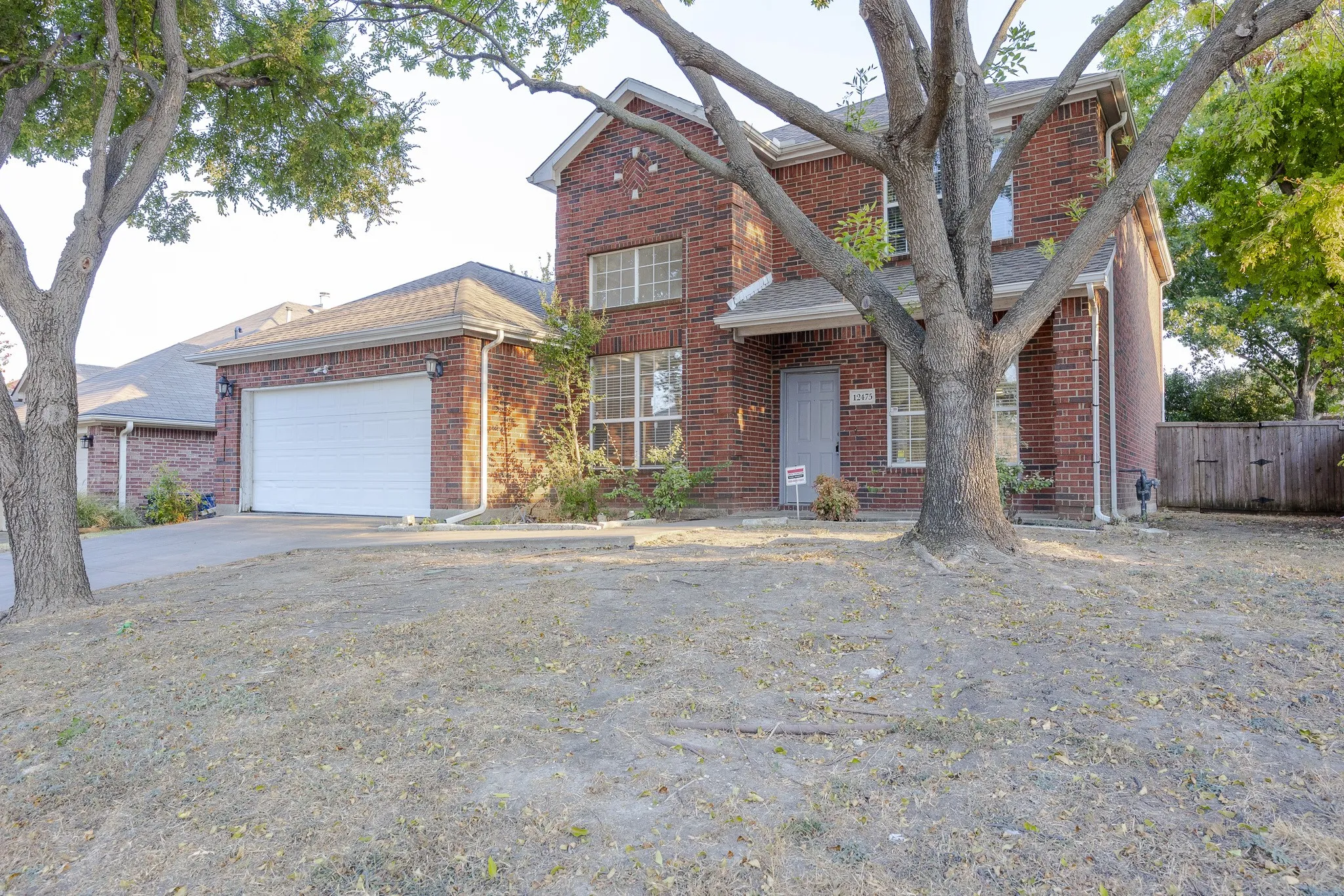 Two-story brick exterior with a two-car garage, front entry door, and a partially fenced yard