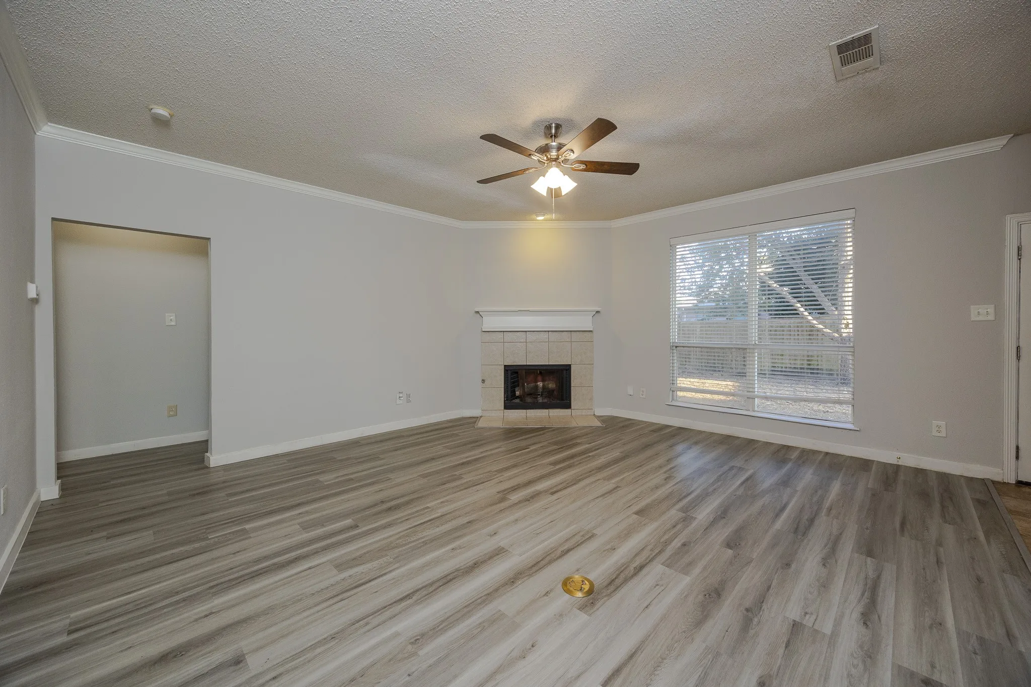 Spacious living area featuring wood-finish flooring, a tiled fireplace with mantel, a ceiling fan with integrated lighting, and crown molding
