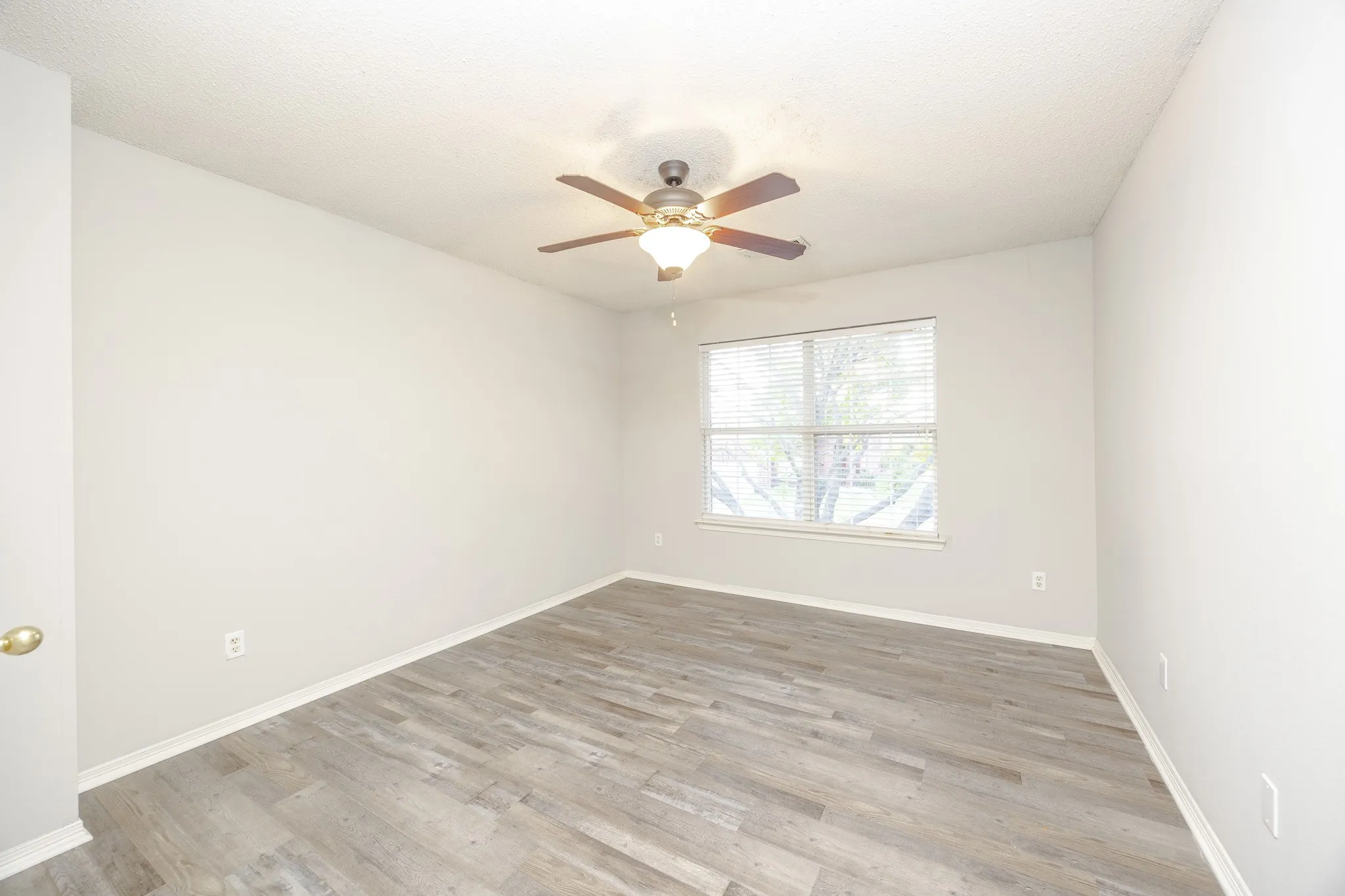 Wood-finish flooring, ceiling fan with integrated lighting, and a window with blinds