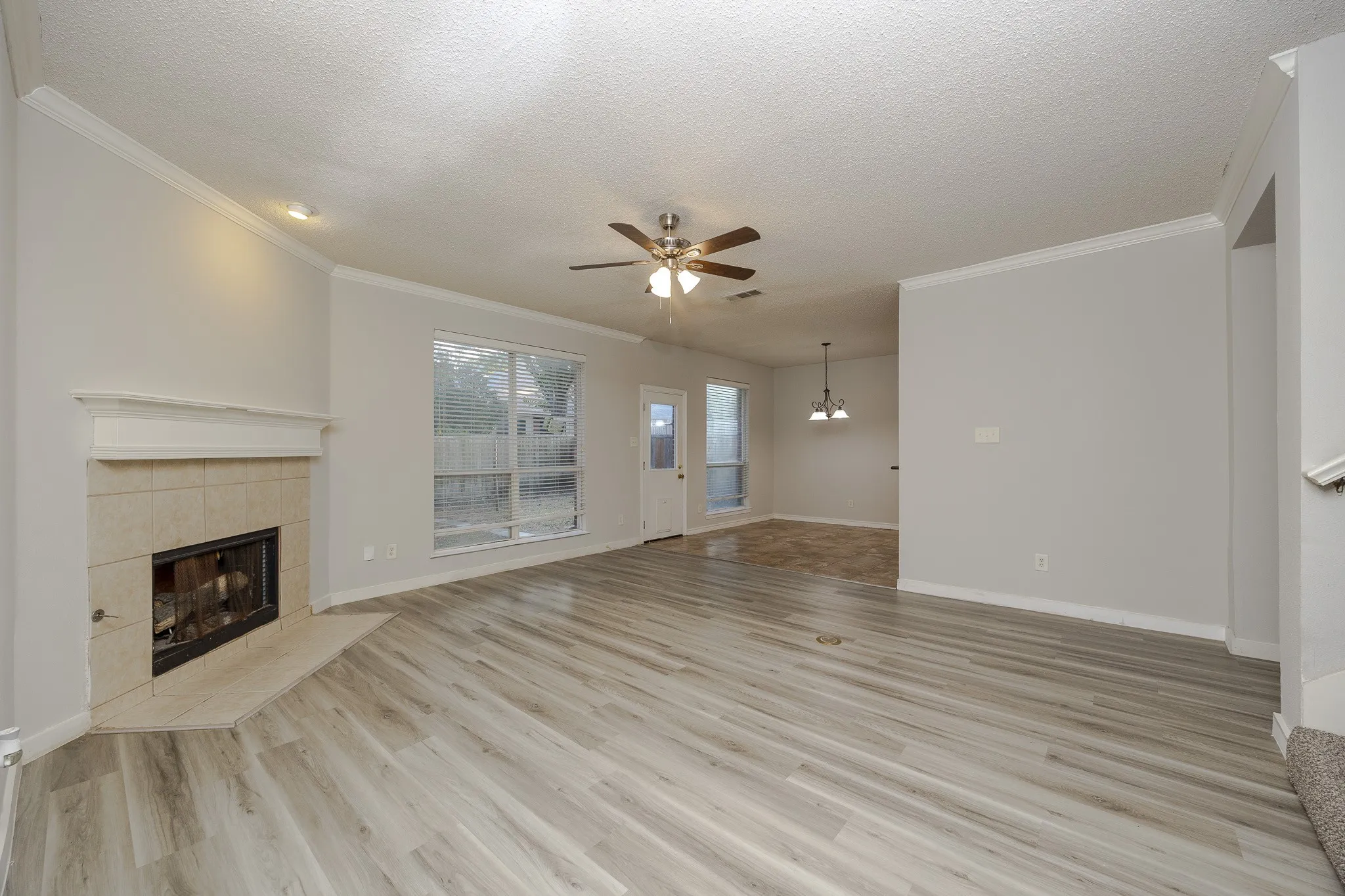 Living space featuring light wood-finish flooring, a tile-surround fireplace with a mantel, a ceiling fan, and a large window