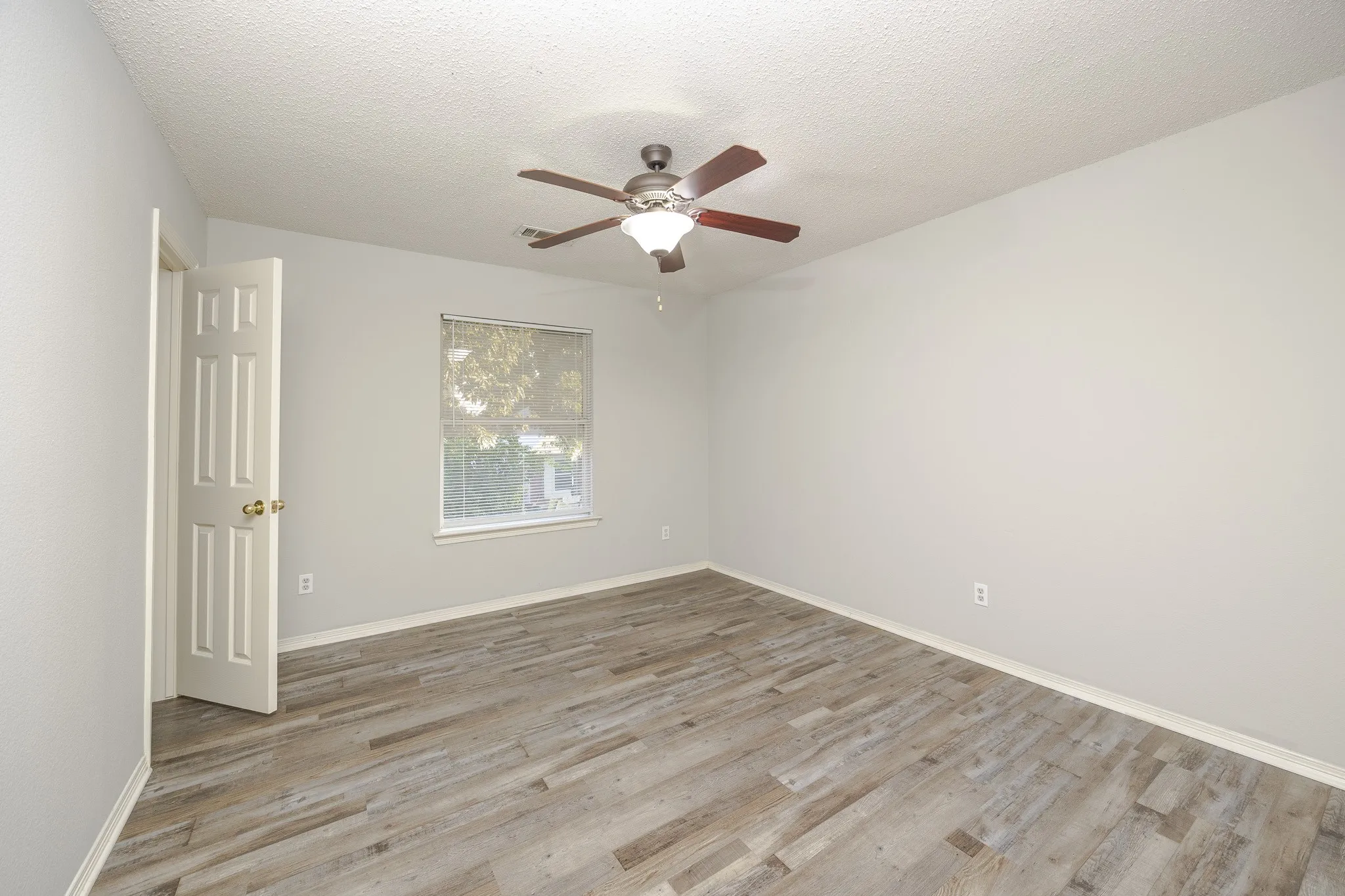 Neutral wall paint with wood-finish flooring, a ceiling fan with integrated lighting, and a window providing natural illumination