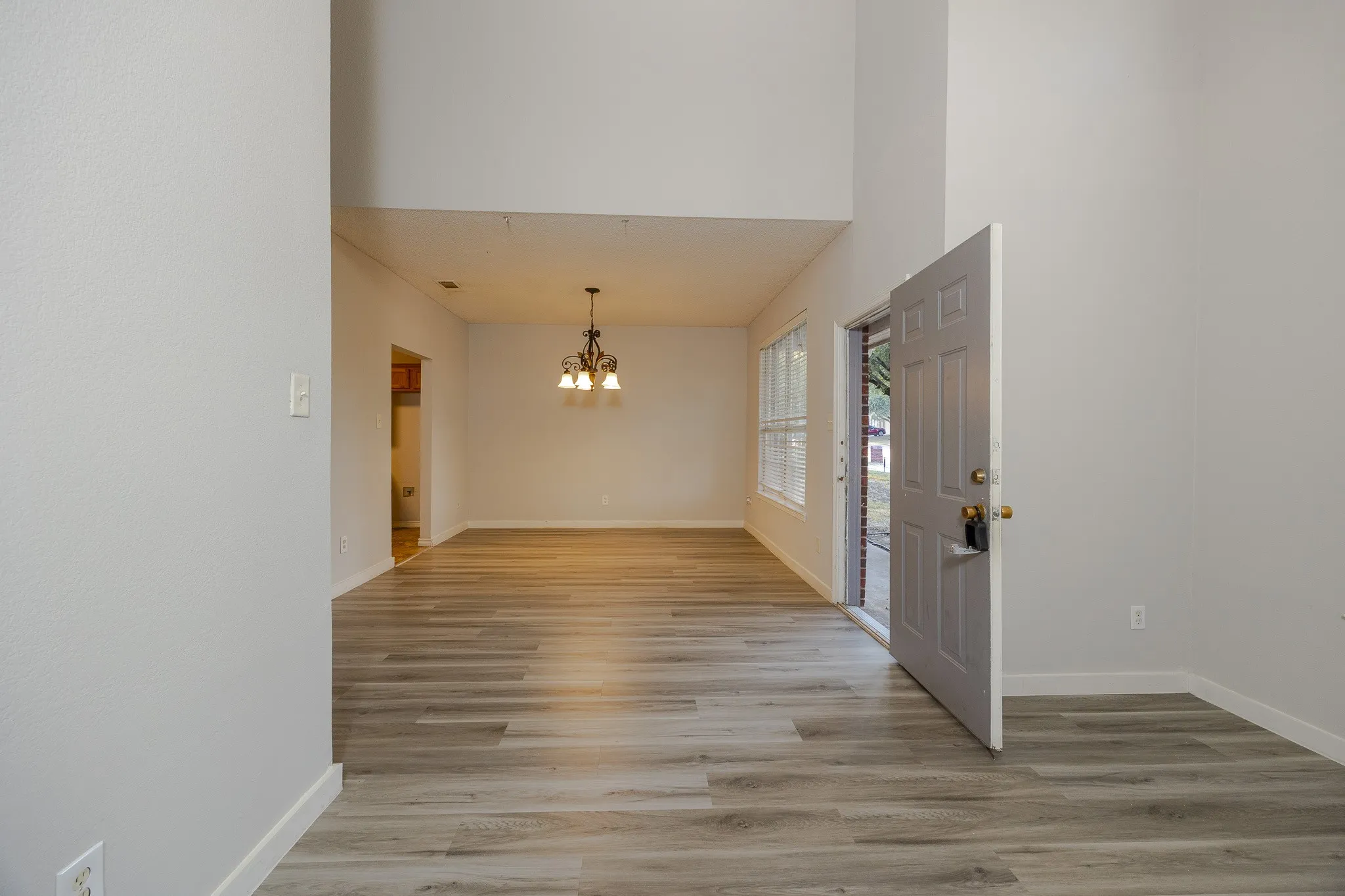 Vaulted ceiling, wood-finish flooring, paneled front door, multi-pane windows, and a chandelier-style light fixture