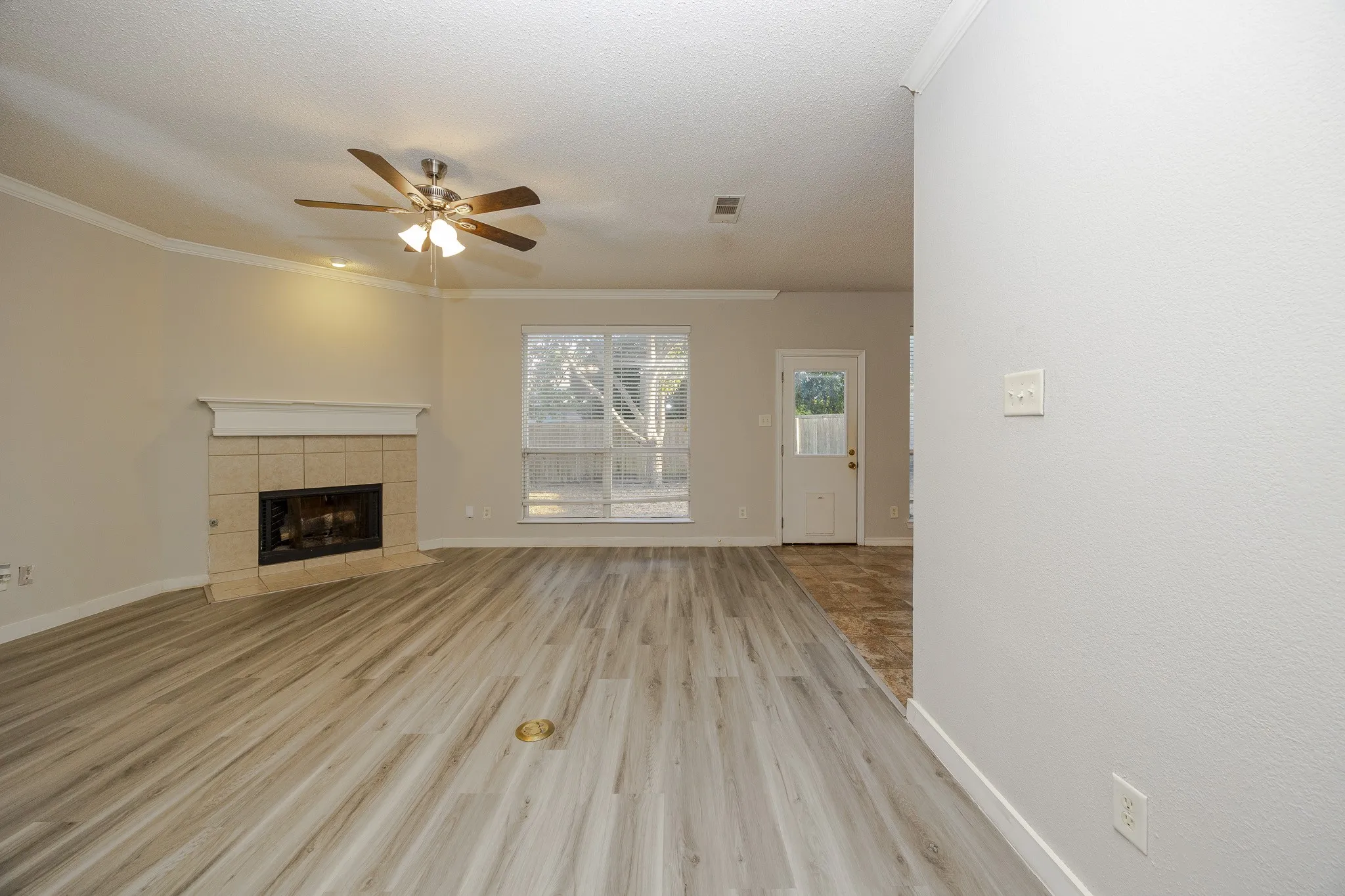 Living area featuring wood-finish flooring, a tile-surround fireplace with a mantel, crown molding, and a ceiling fan with integrated lighting