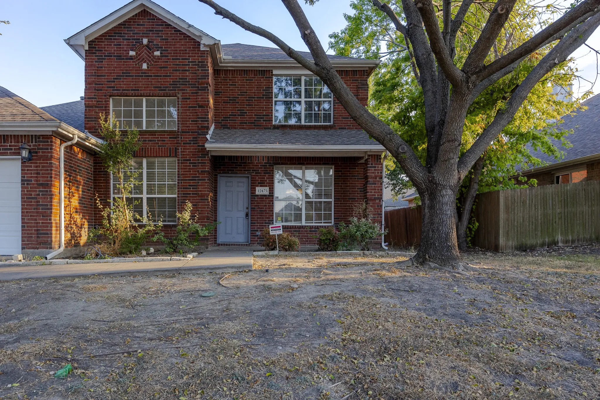 Brick facade residence featuring multiple windows, an attached garage, and a mature front yard tree