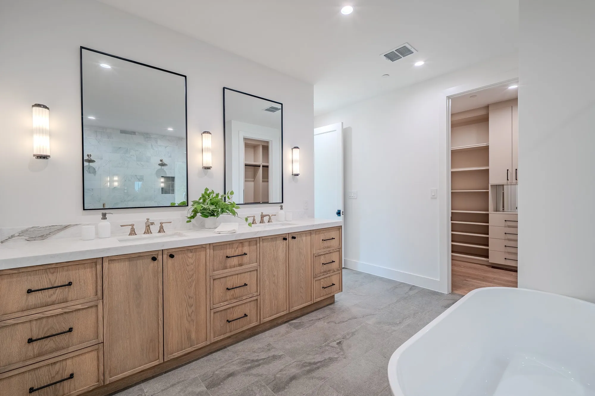 Bathroom featuring double vanity, a tile shower, a freestanding bath, a walk in closet, and recessed lighting