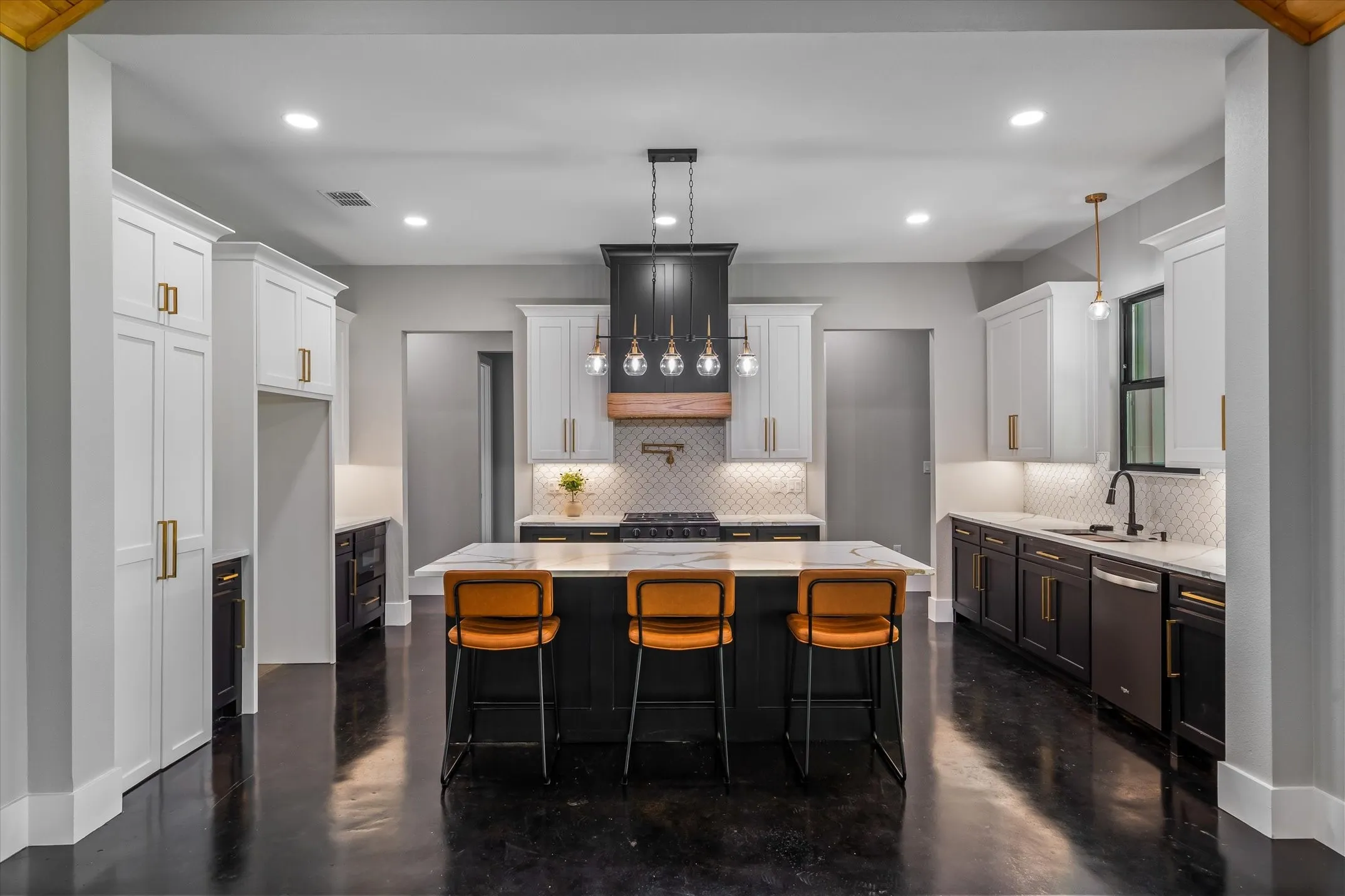 Spacious kitchen featuring a central island with countertop seating, white and dark-toned cabinetry with gold-finish hardware, stainless steel appliances, and a tile backsplash