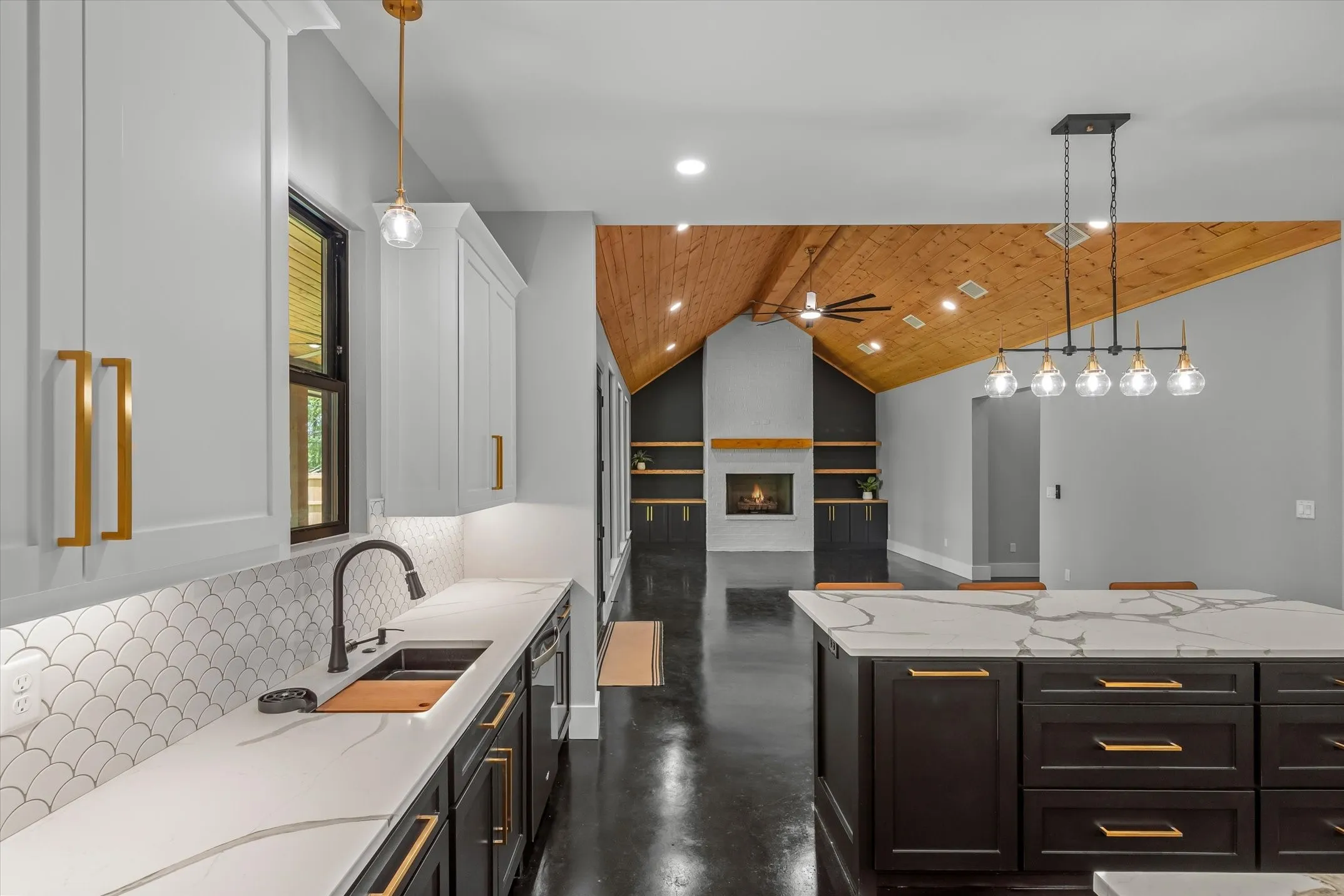 Modern kitchen featuring white shaker upper cabinetry and dark lower cabinetry, quartz countertops with a waterfall edge, a scalloped tile backsplash, and a black sink with a matte black faucet