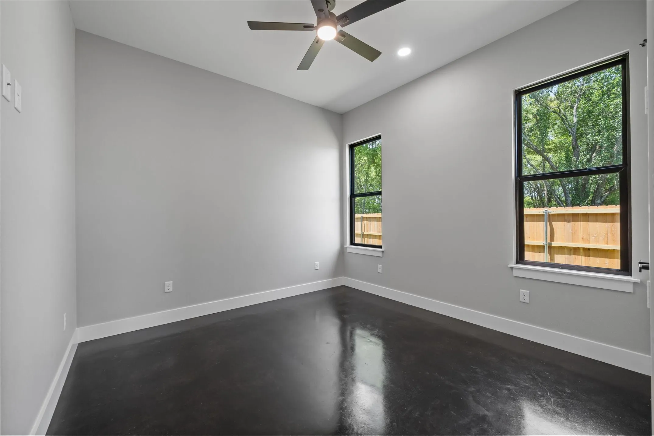 Spacious room featuring dark polished concrete flooring, white baseboards, and light gray walls