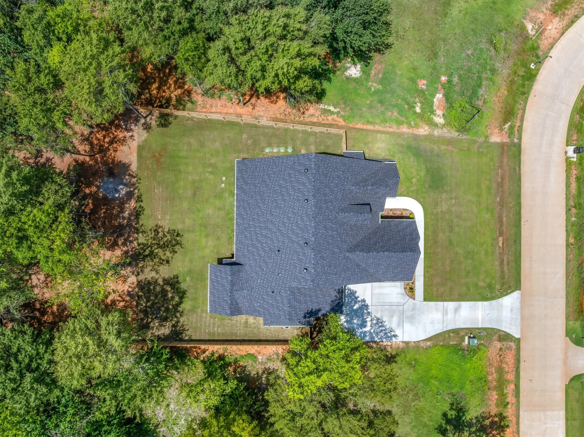 Aerial view showcasing a newly constructed home with a dark shingle roof, concrete driveway, and expansive green lawn