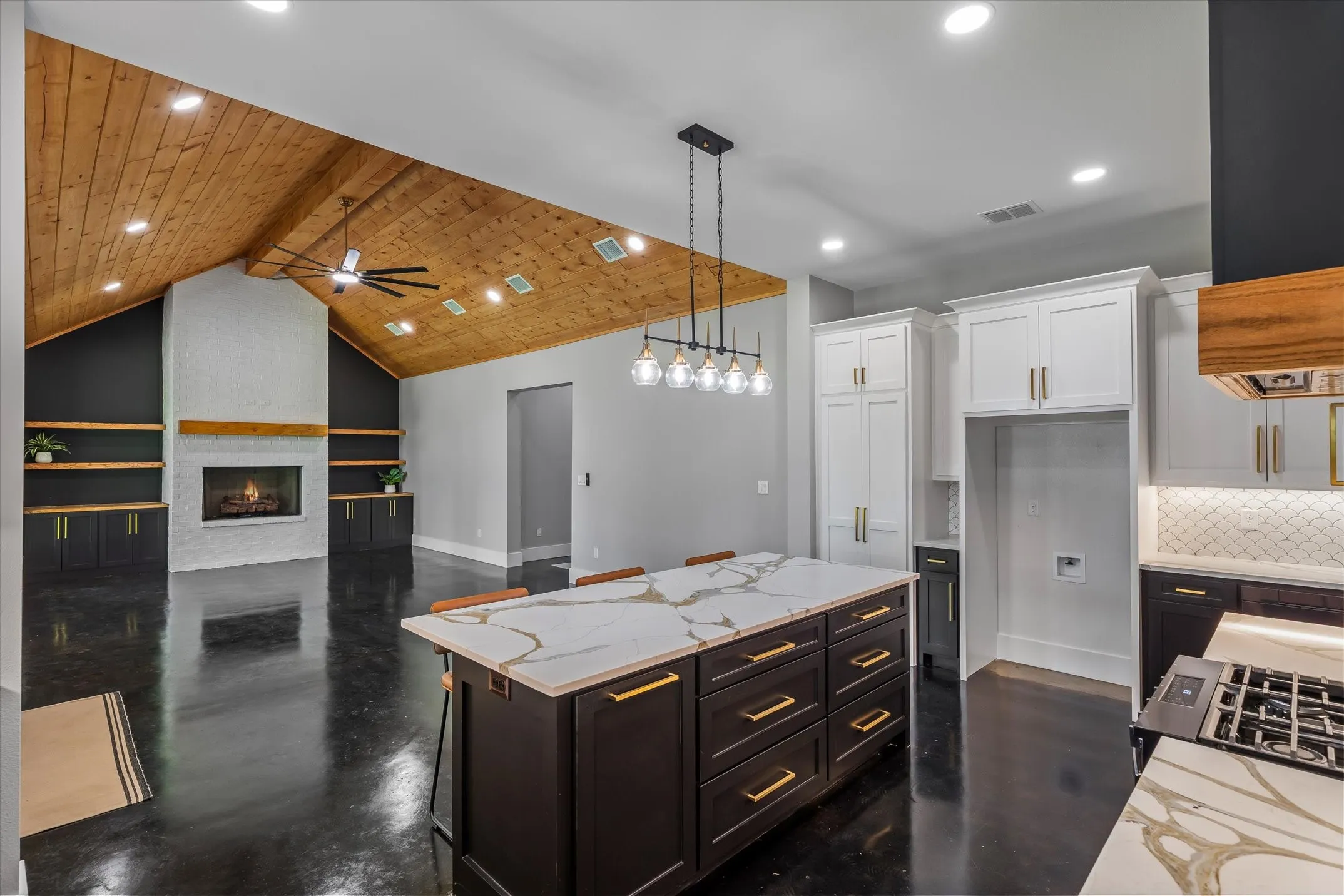 Open-concept living space featuring a vaulted wood-plank ceiling, white brick fireplace with wood mantel, and built-in shelving