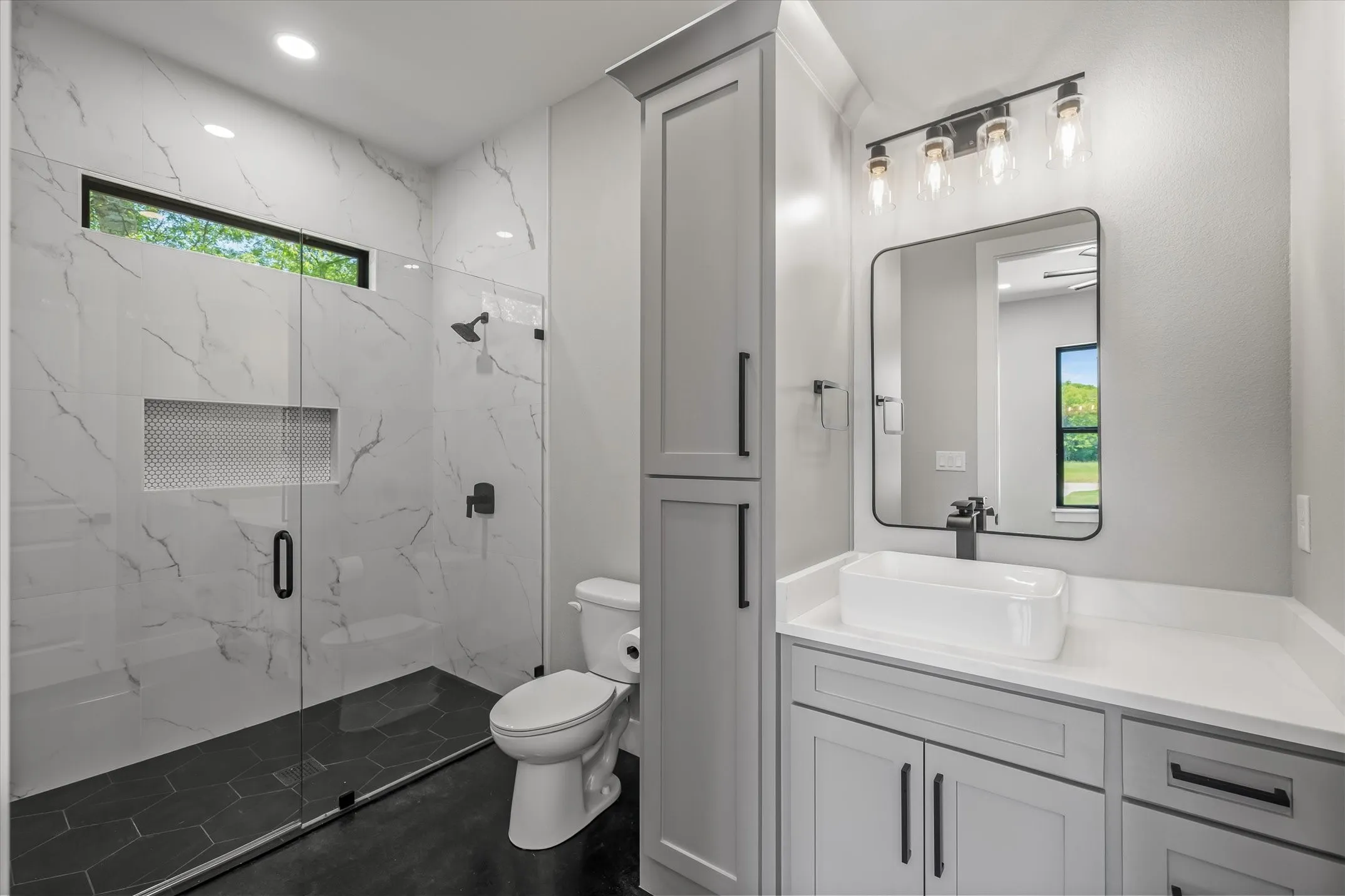 Contemporary bathroom featuring a spacious walk-in shower with white marble-look tile, black hexagonal floor tile, and a transom window
