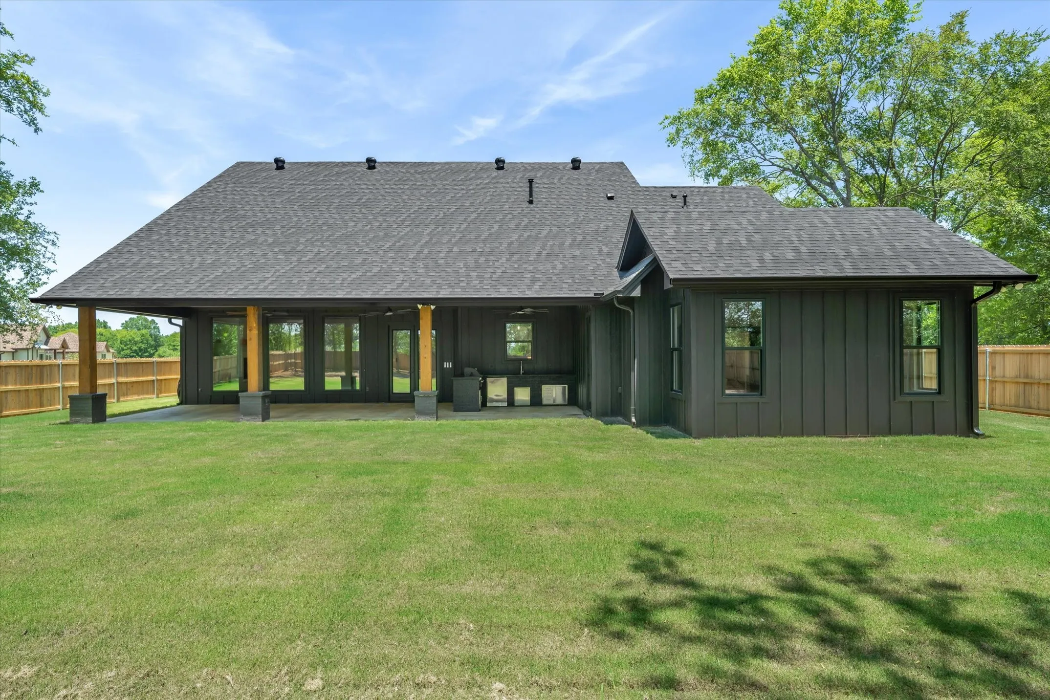 Expansive backyard with a manicured lawn, featuring a covered patio, outdoor kitchen, and dark gray board and batten siding