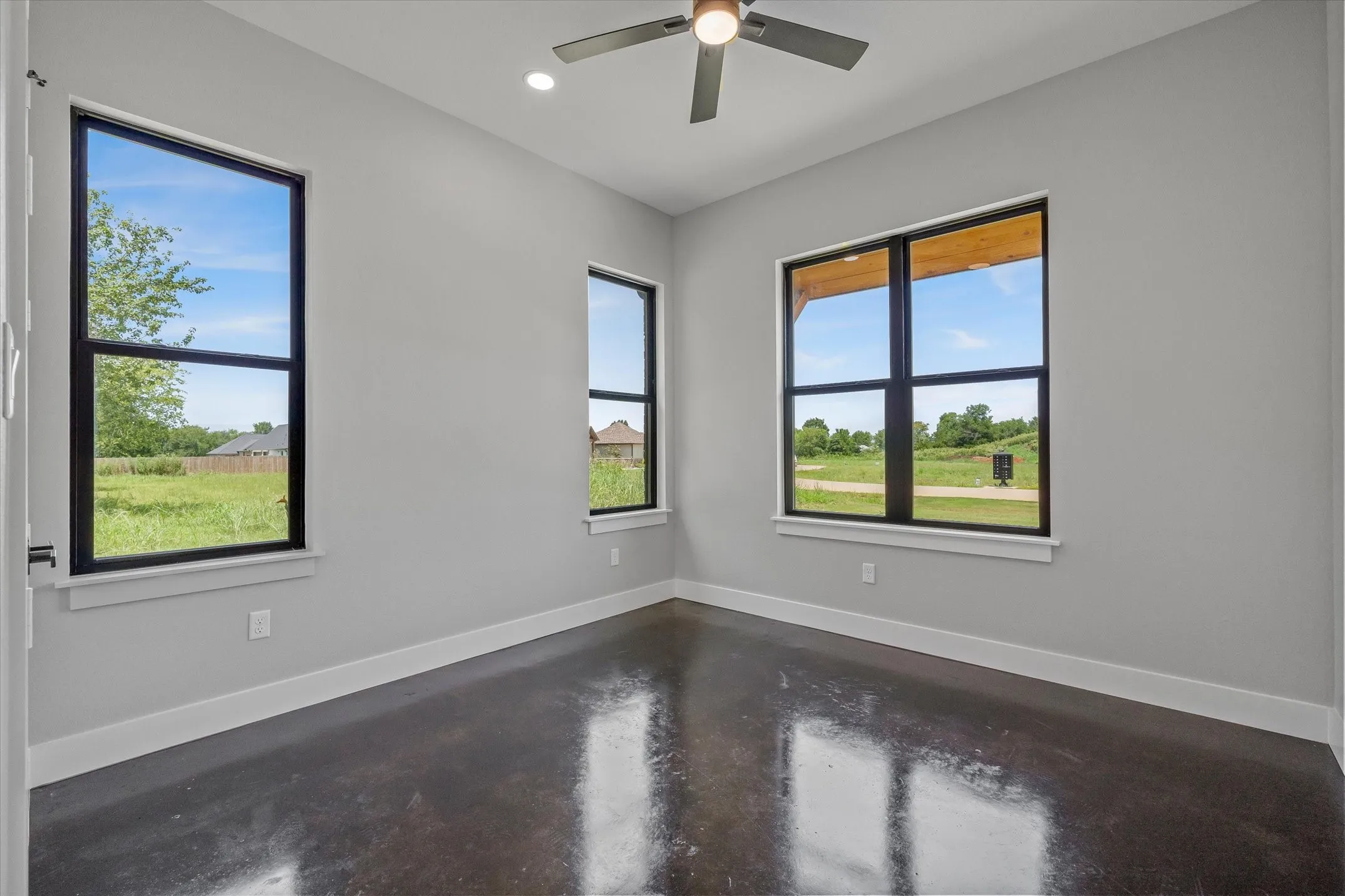 Spacious room featuring multiple large windows with black frames, offering expansive views of surrounding green space