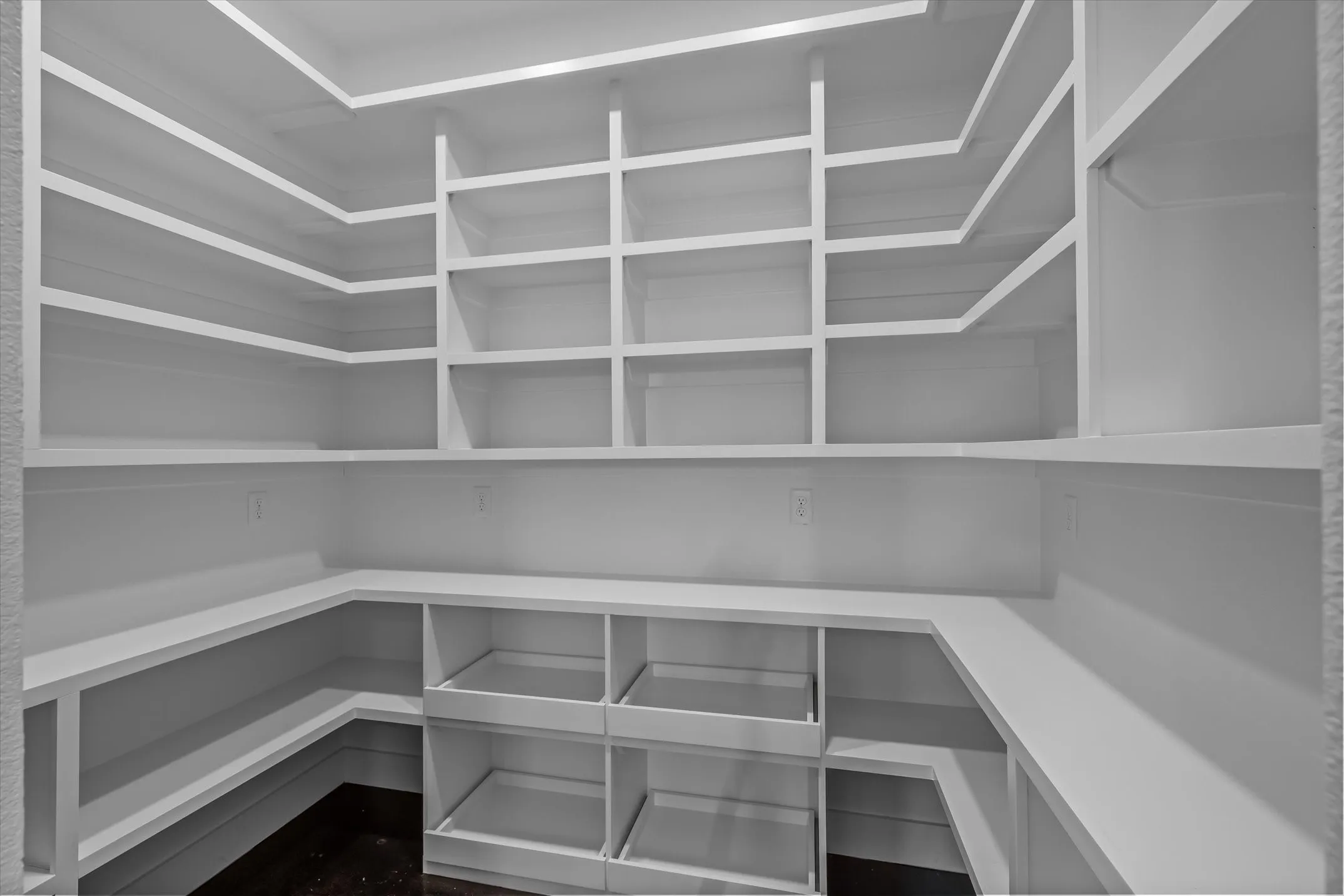 Walk-in pantry featuring white shelving, built-in lower storage, and dark wood-finish flooring