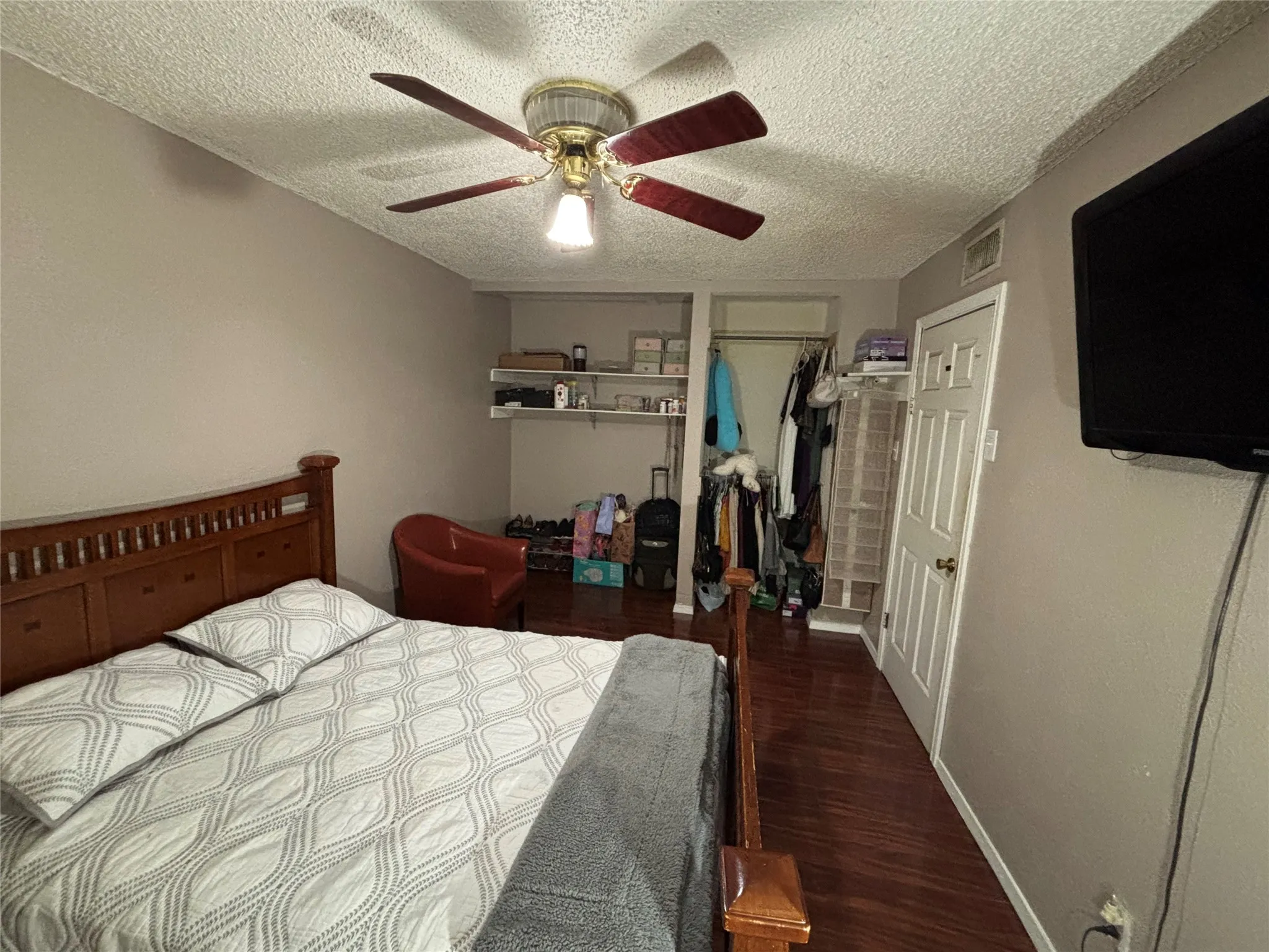 Master bedroom featuring wood-finish flooring, a ceiling fan with integrated lighting, and a built-in open-shelf storage system