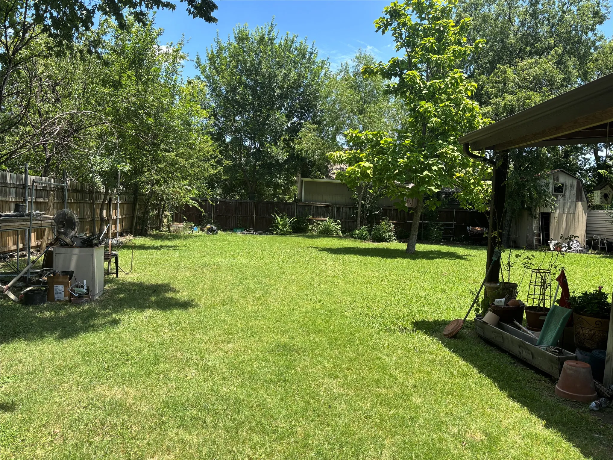 Grassy yard with mature perimeter trees, a wood privacy fence, and a storage shed