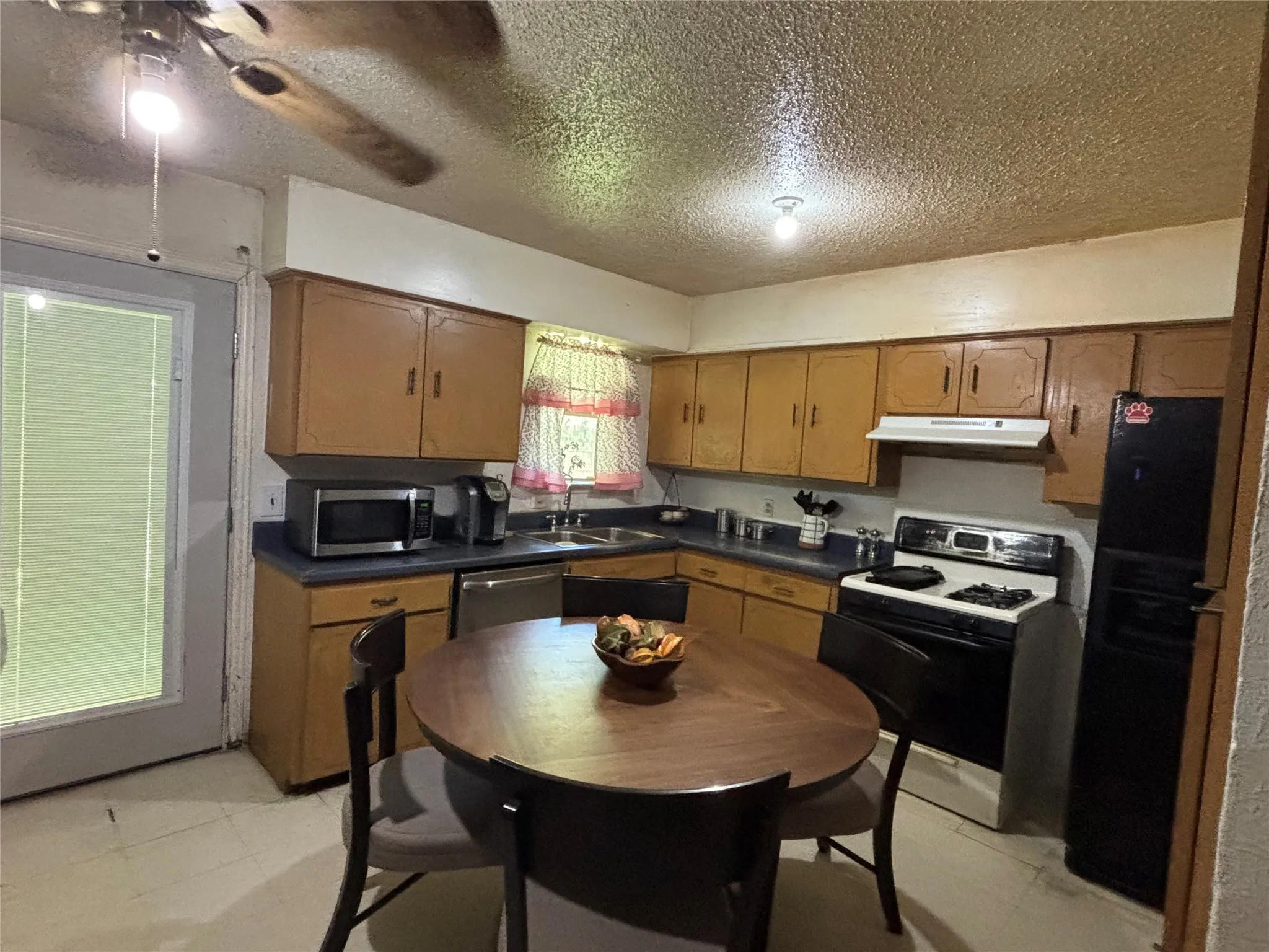 Kitchen featuring wood cabinetry, dark countertops, a built-in range hood, and a ceiling fan