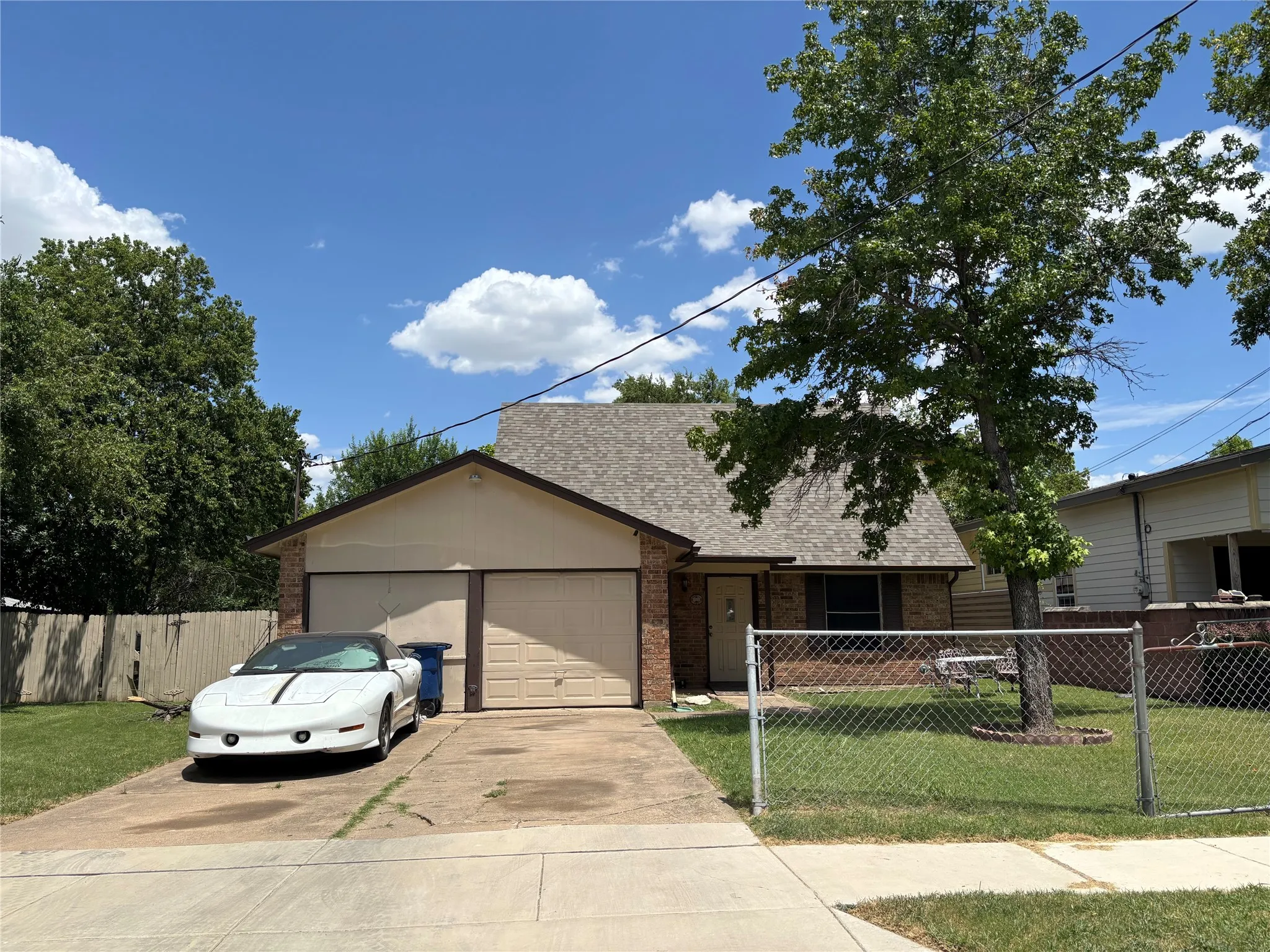 Brick facade home with a two-car garage, concrete driveway, and mature front yard tree