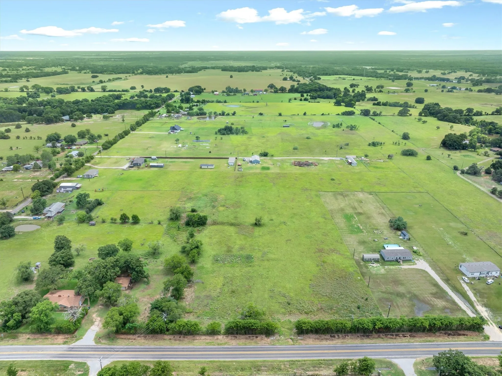 Expansive aerial property featuring vast green acreage, scattered mature trees, and visible road frontage