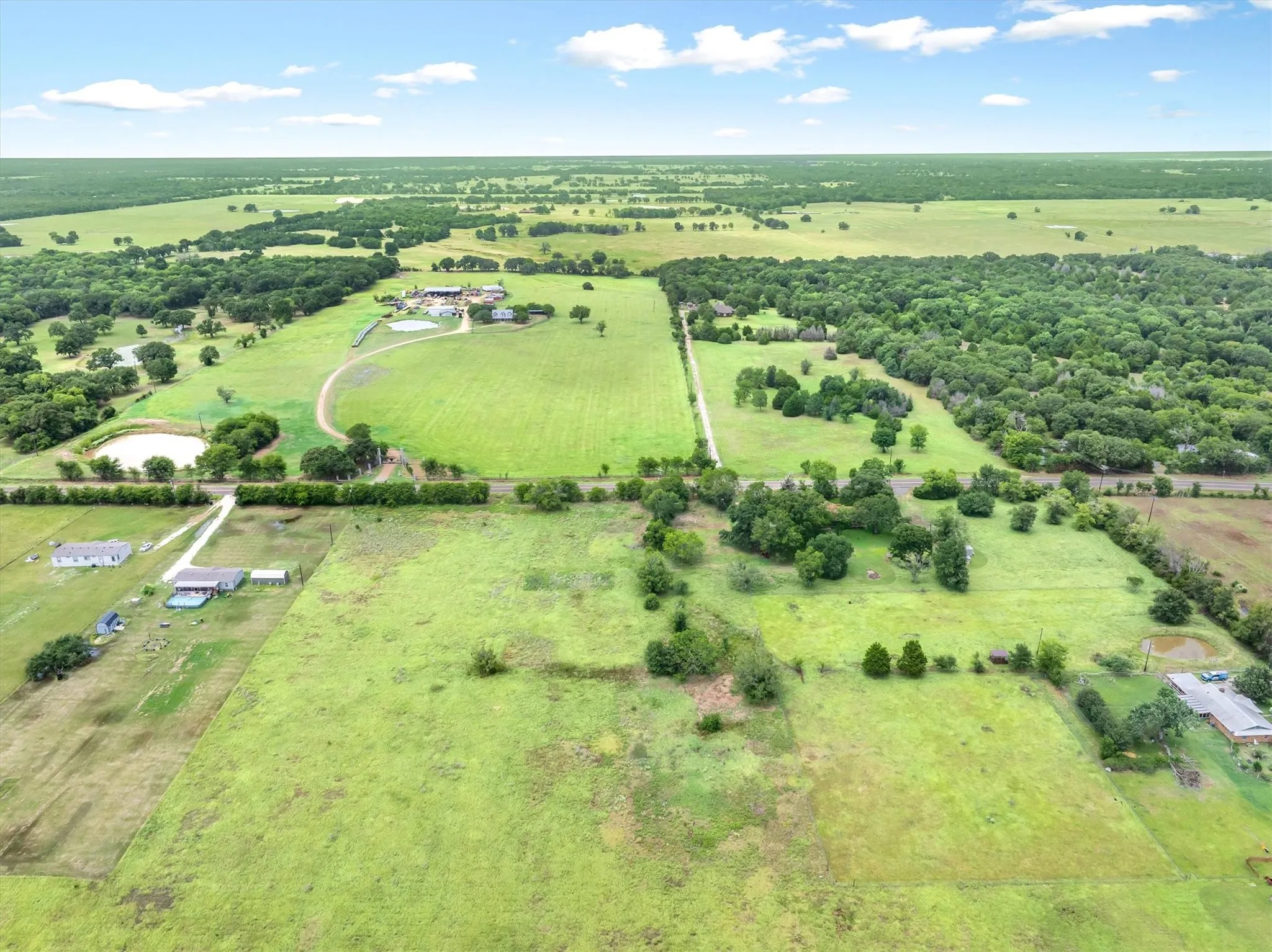 Expansive property featuring vast open fields, mature tree lines, multiple residential structures, a private pond, and extensive undeveloped acreage
