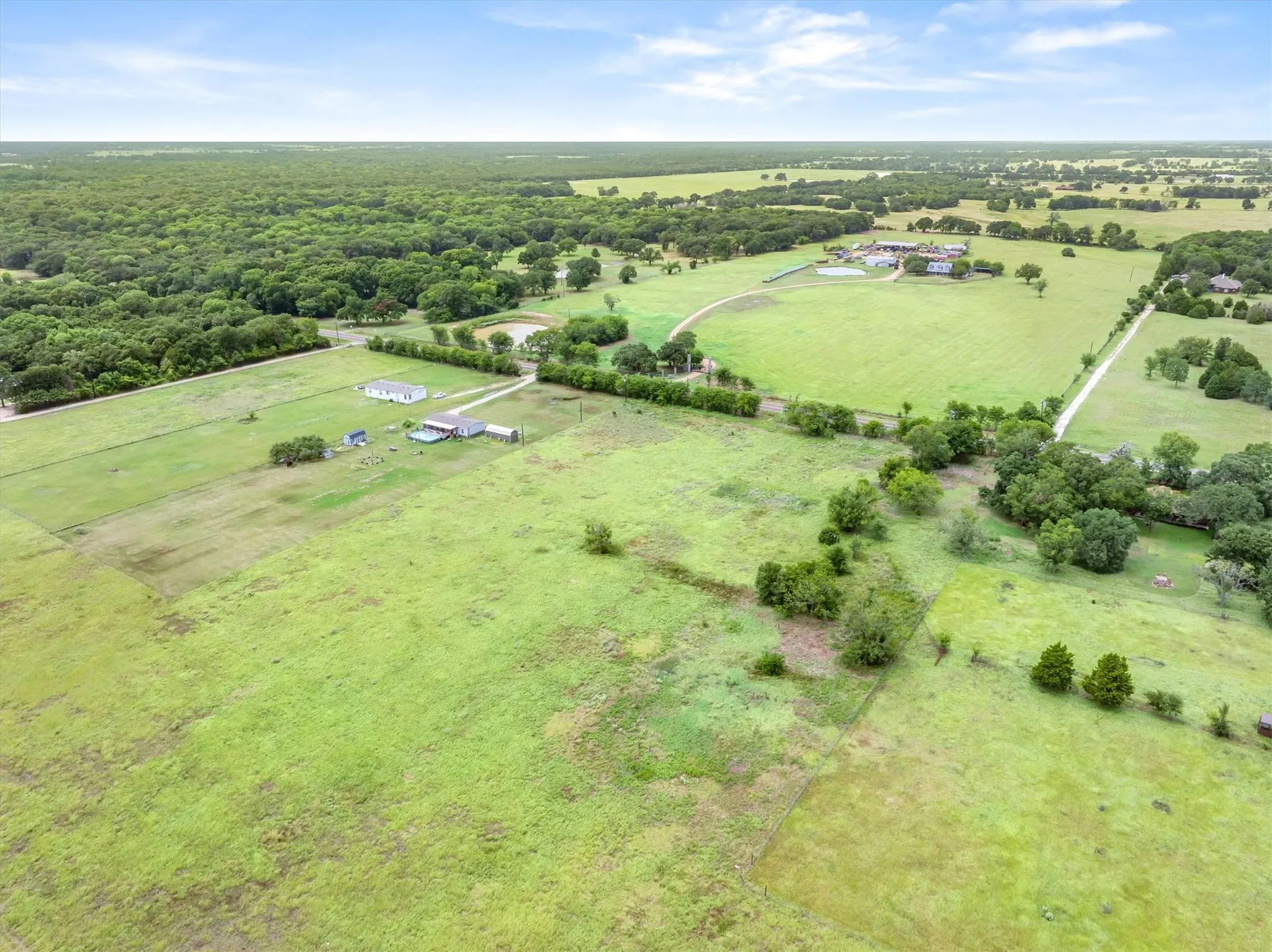 Expansive rural property featuring multiple pastures, mature trees, a natural pond, and distant structures