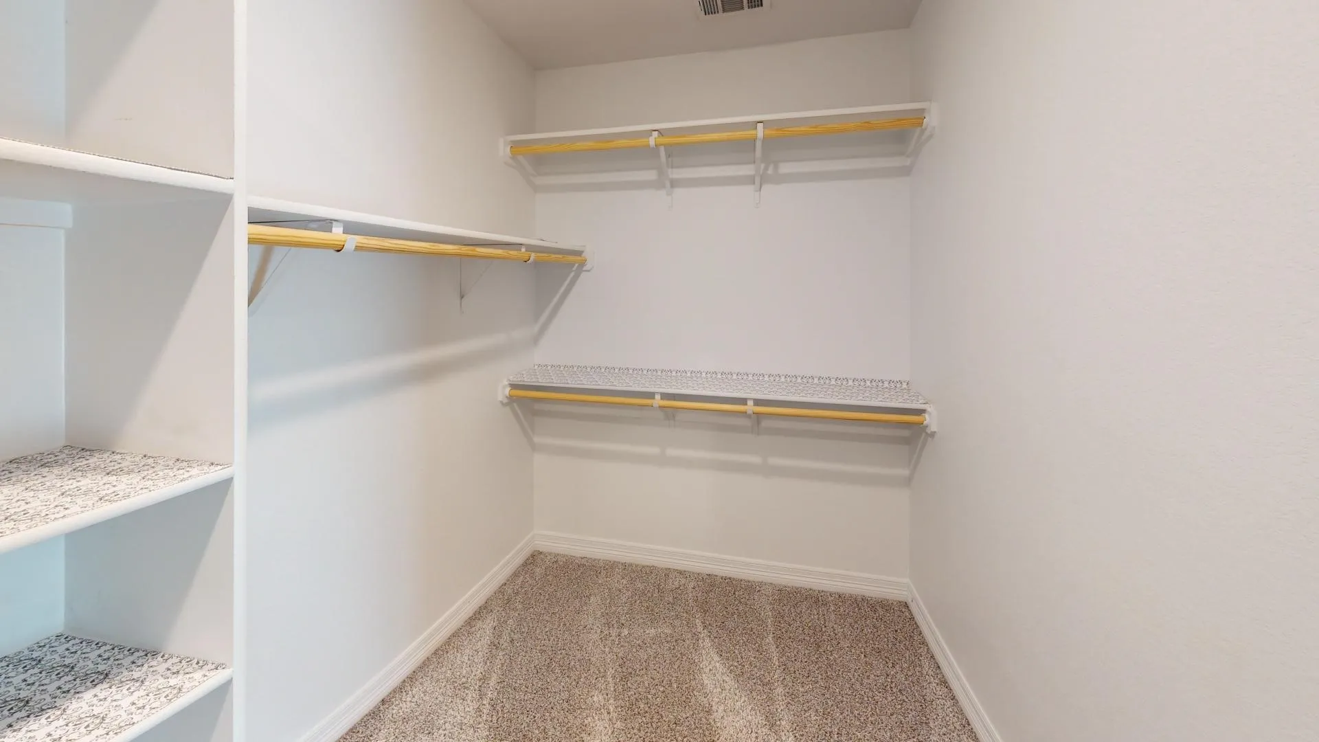 Spacious walk-in closet in first primary bedroom featuring built-in shelving, multiple hanging rods, white walls, and neutral carpeting