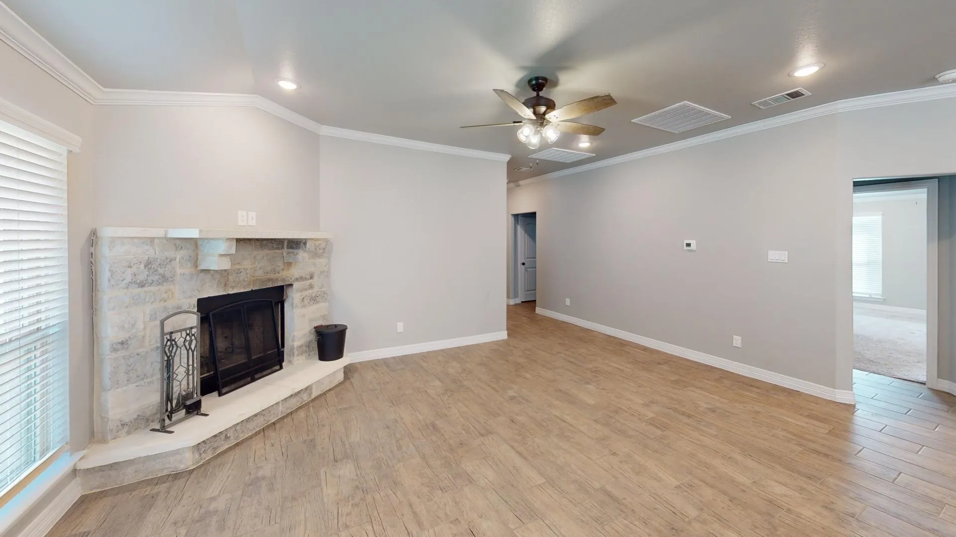 Spacious room featuring wood-look tile flooring, a corner stone fireplace with a raised hearth, recessed lighting, and a ceiling fan