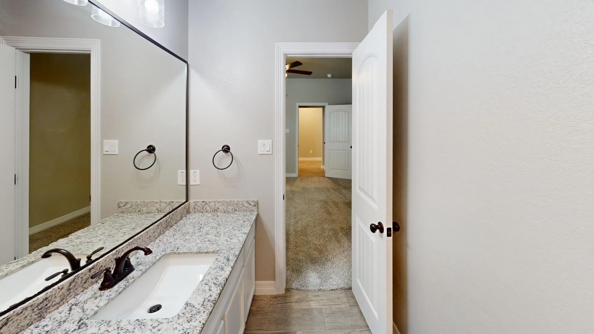 Second primary bathroom vanity featuring dual sinks with dark bronze fixtures, a speckled countertop, and an elongated mirror
