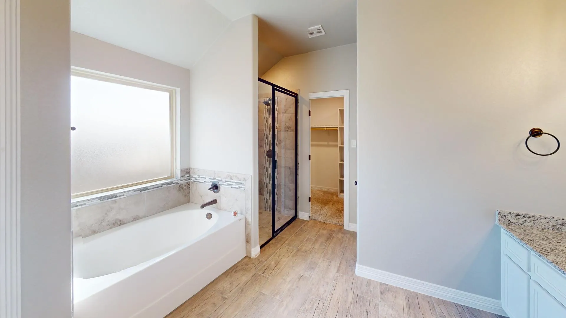 Bathroom featuring a soaking tub with tile surround, a separate glass-enclosed shower, wood-finish flooring, and a vanity with a granite countertop