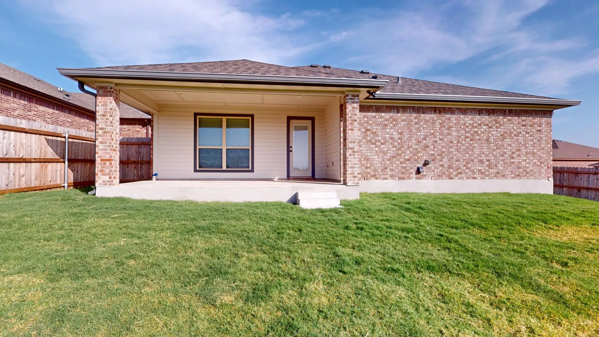 Backyard featuring a covered patio, a concrete slab, and a green lawn