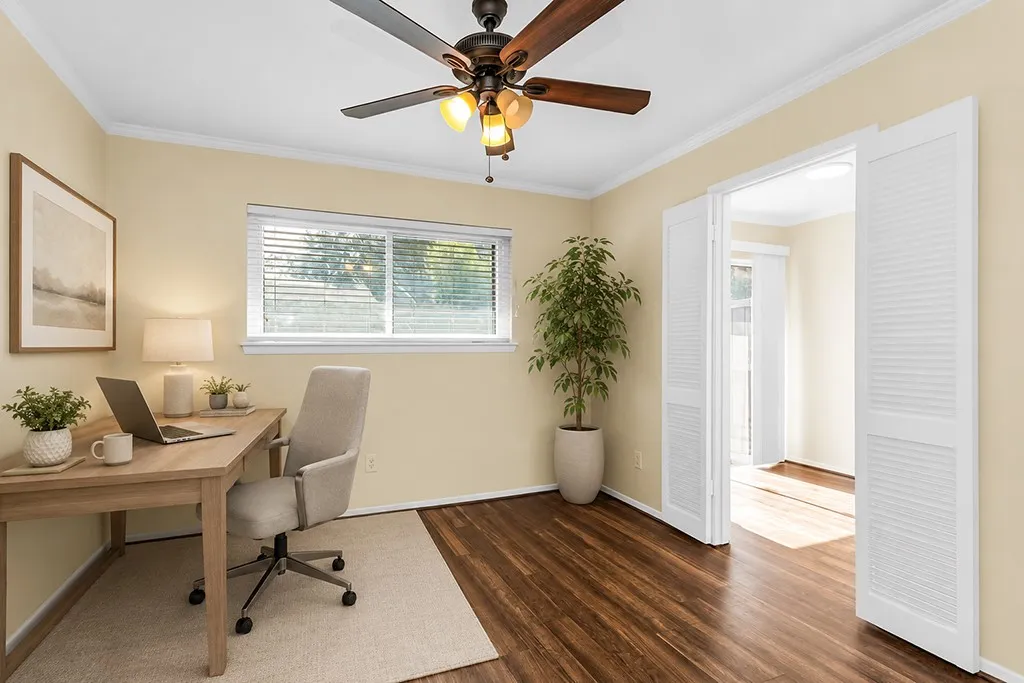Virtually staged Bedroom #3 shown as an office.  Room featuring wood-finish flooring, a ceiling fan with light fixture, white louvered bifold doors, a window with horizontal blinds, and crown molding