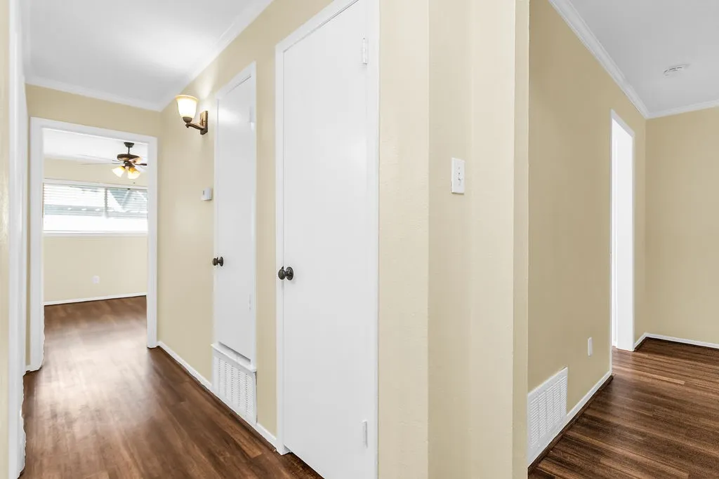 Hallway featuring wood-finish flooring, light-toned wall paint, white trim, and white interior doors with dark hardware
