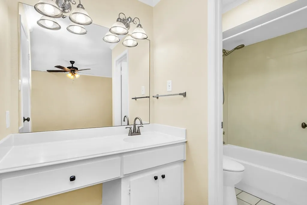 Bathroom featuring a vanity with an integrated sink, a rectangular mirror, a chrome light fixture, a toilet, and a bathtub with shower