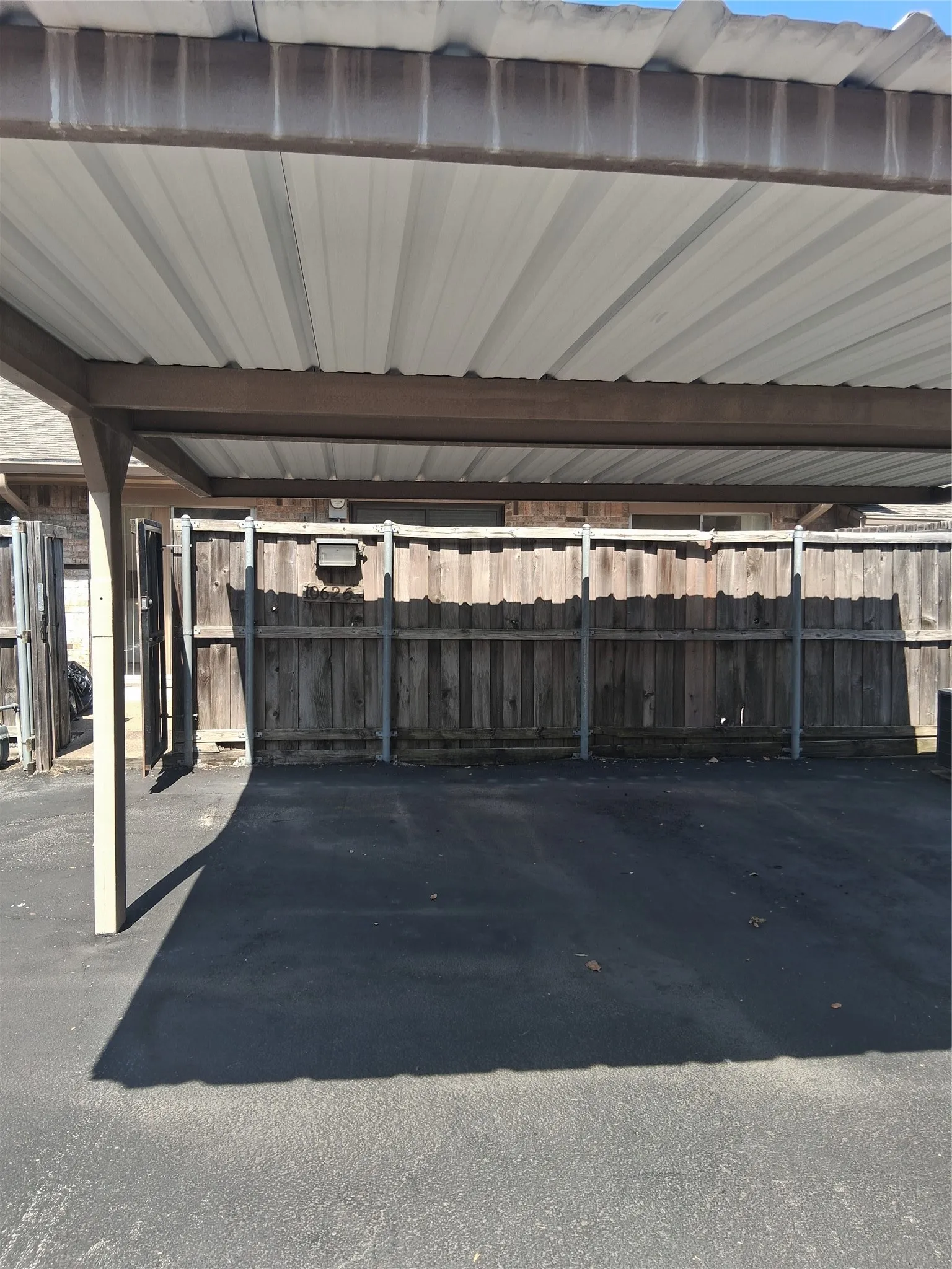 Carport structure featuring a corrugated metal roof and exposed support beams Gate to patio is open on the left.