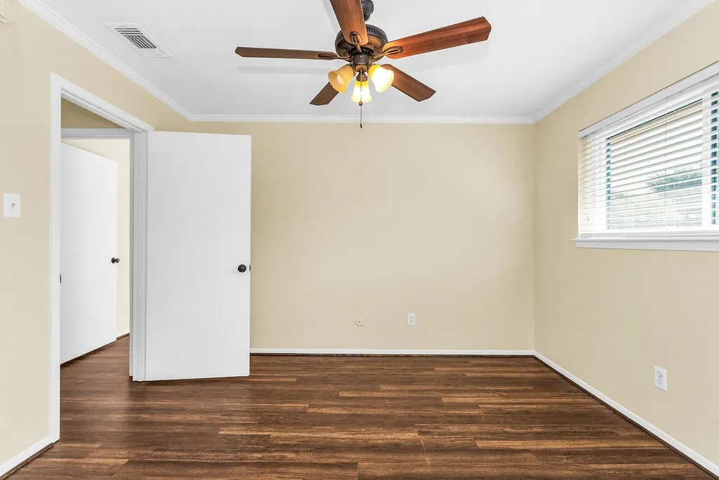 Interior room #3 featuring wood-finish flooring, a ceiling fan with integrated lighting, a window with horizontal blinds, and two paneled doors with black hardware