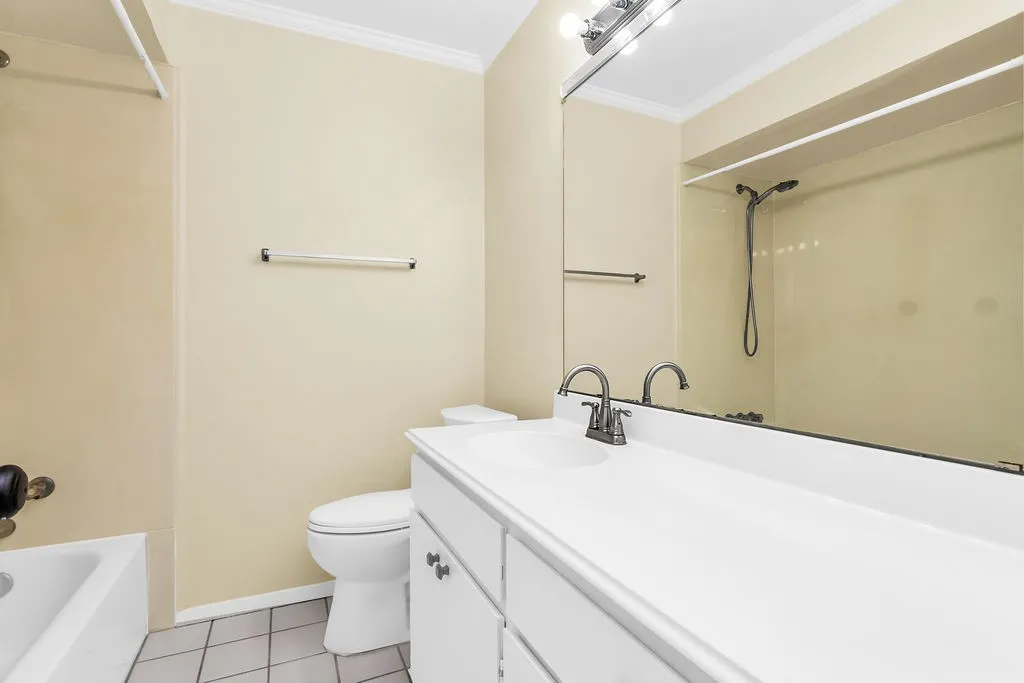Bathroom featuring a white vanity with integrated sink, brushed nickel faucet, large wall-mounted mirror, and white tiled flooring