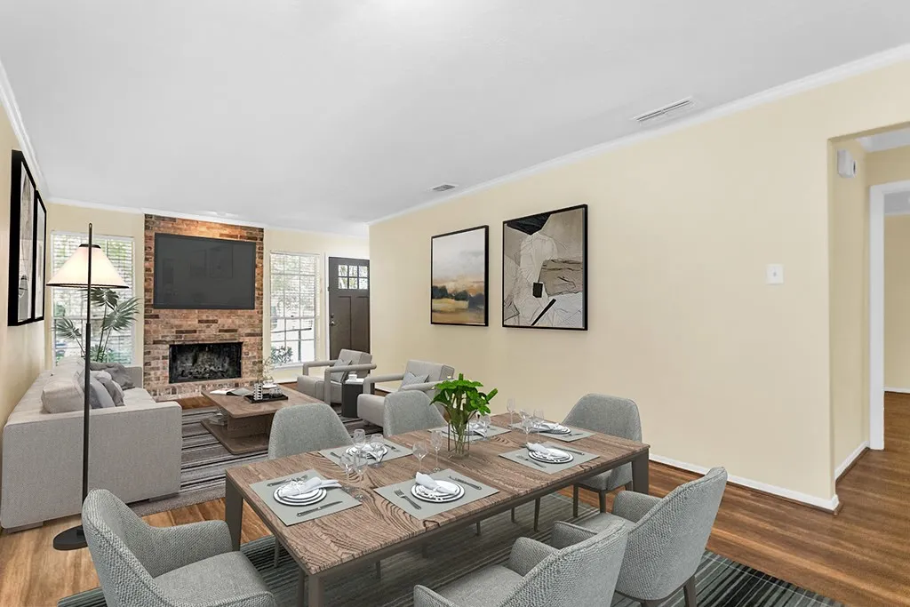 Virtually staged Open-concept living area featuring wood-finish flooring, a brick fireplace with a hearth, crown molding, and a solid wood entry door with glass inserts
