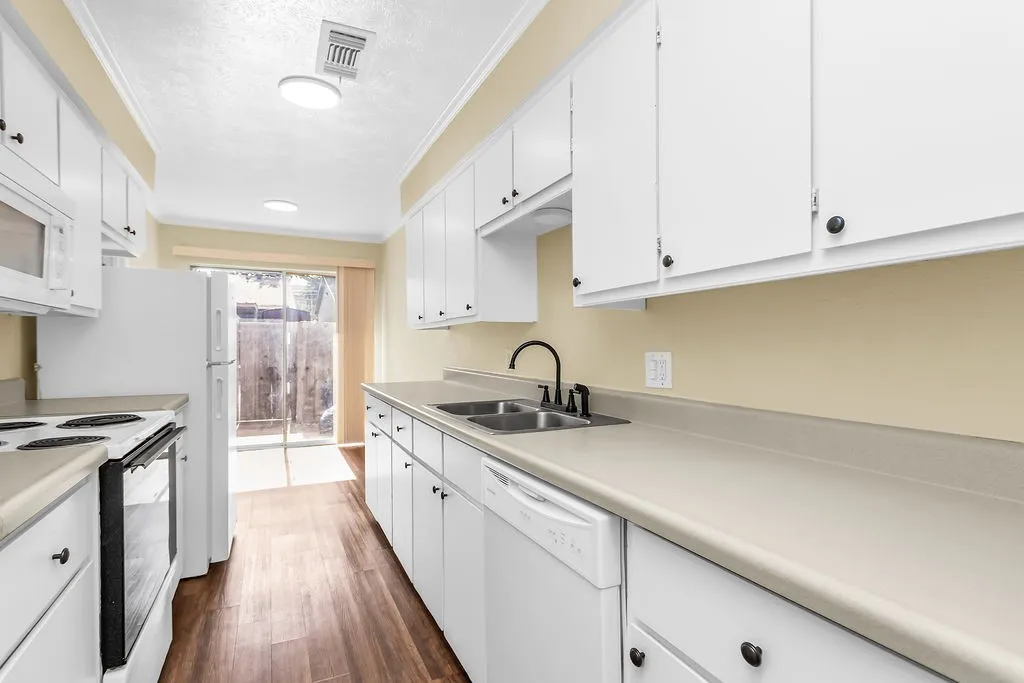 Galley kitchen featuring white cabinetry, light countertops, wood-finish flooring, white appliances, and a sliding glass door