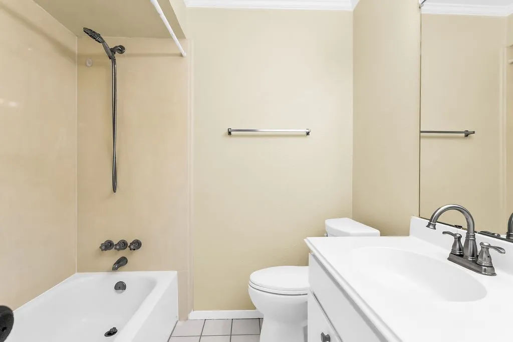 Bathroom featuring a white bathtub with dark fixtures, a white vanity with an integrated sink, a large wall-mounted mirror, and tile flooring