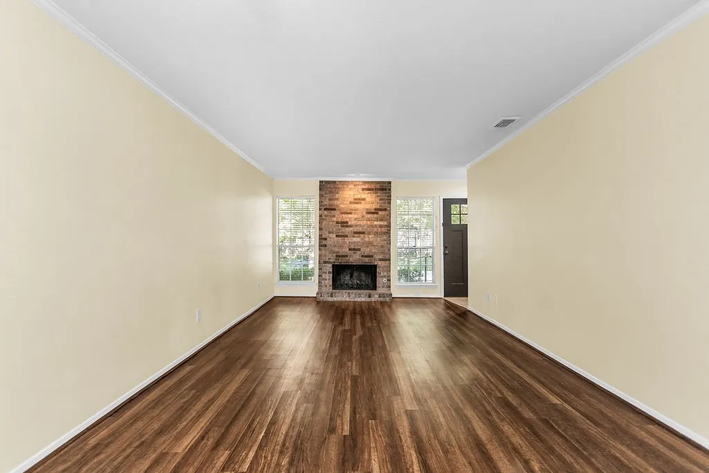 Spacious room featuring wood-finish flooring, a brick fireplace, and two large windows