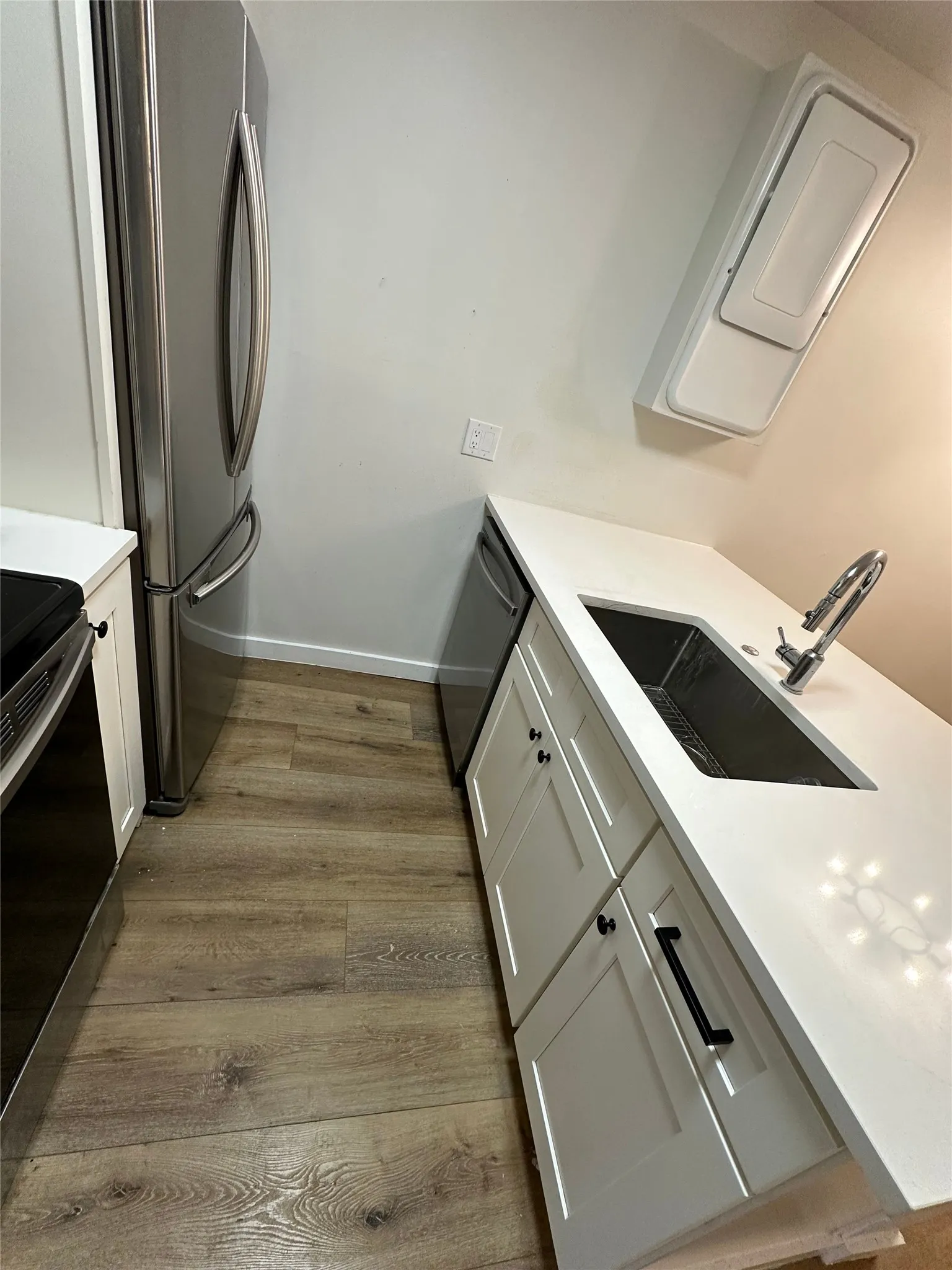 Kitchen featuring white shaker-style cabinetry with matte black hardware, light-toned wood-finish flooring, a stainless steel refrigerator, and a built-in stainless steel dishwasher