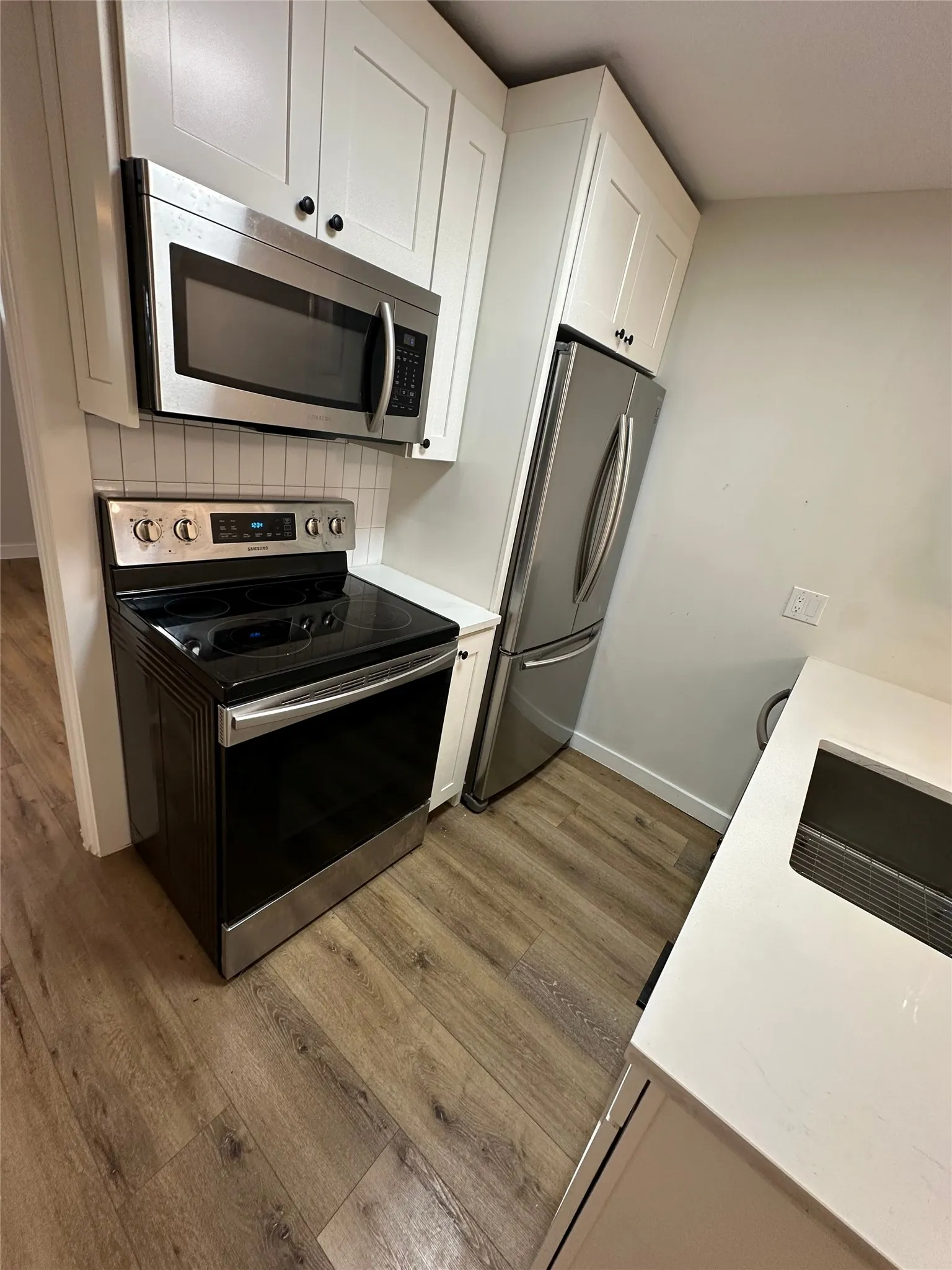 Kitchen featuring stainless steel appliances, white shaker cabinetry, subway tile backsplash, solid surface countertops, and wood-finish flooring