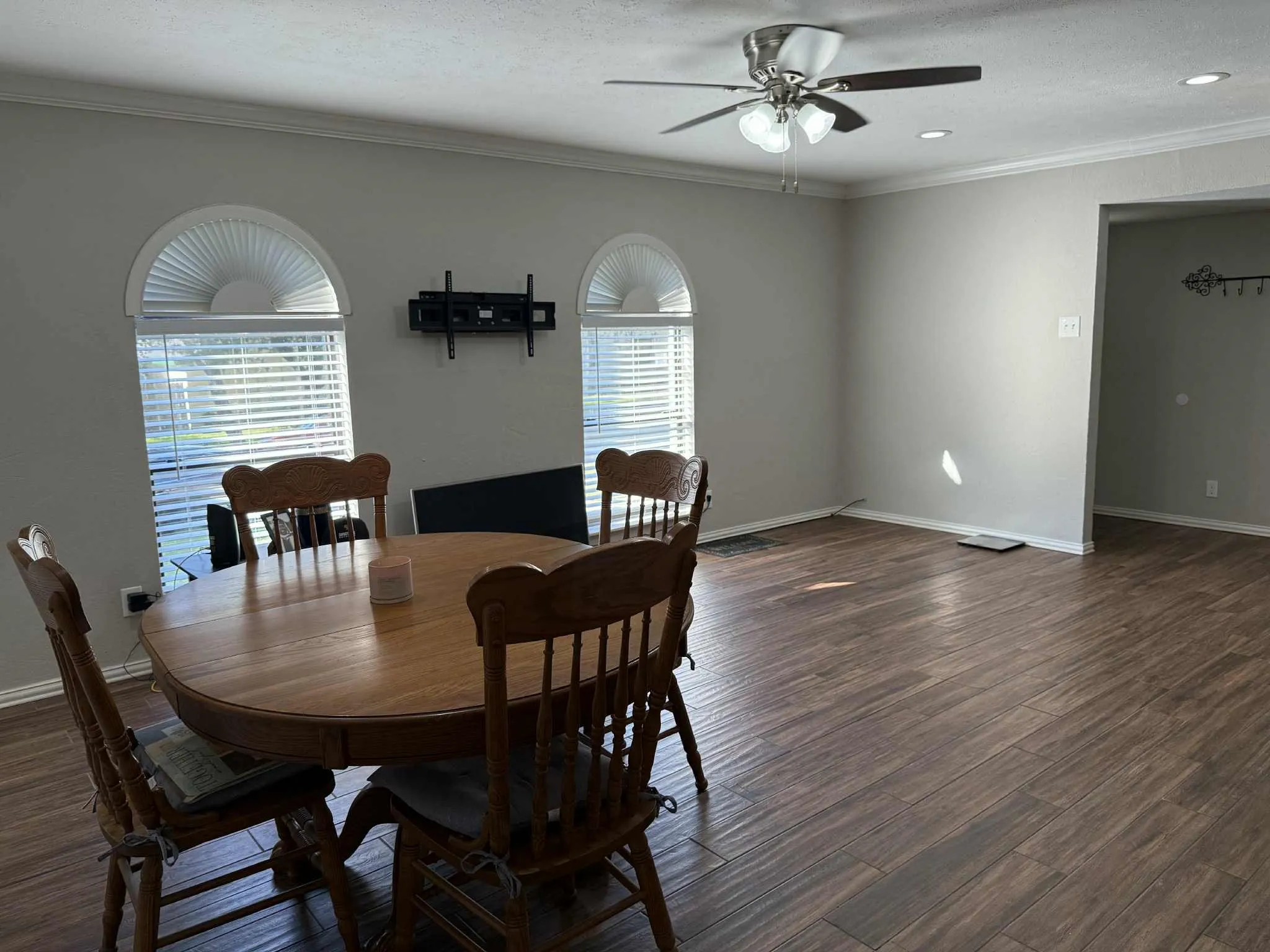 Spacious interior featuring wood-finish flooring, two arched windows with blinds, a ceiling fan with light fixture, recessed lighting, and crown molding