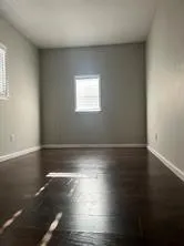 Spacious room with dark wood-finish flooring, two windows with blinds, light gray wall paint, and white baseboards