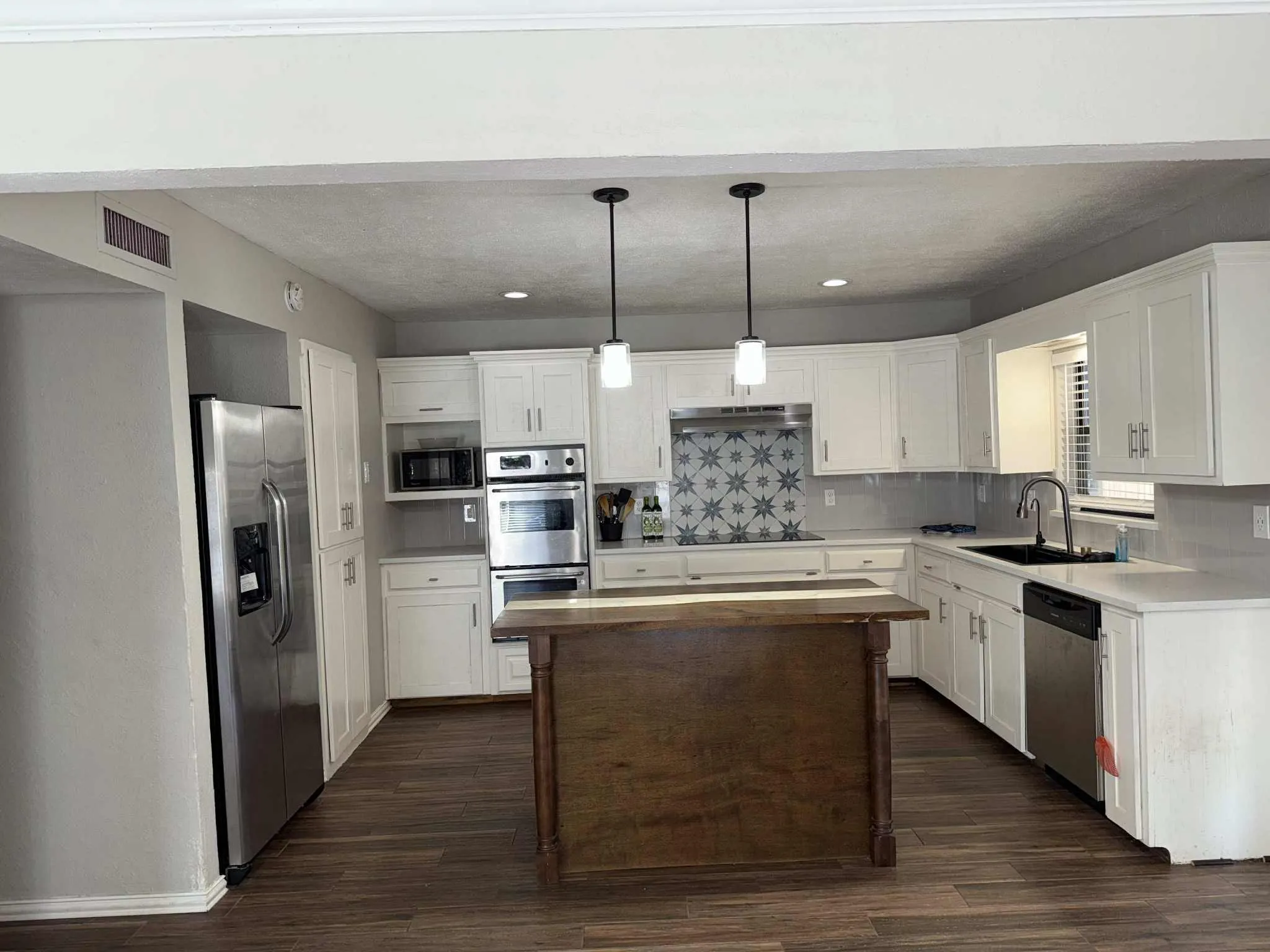 Modern kitchen featuring white cabinetry, stainless steel appliances, a wood-finish island, and patterned tile backsplash