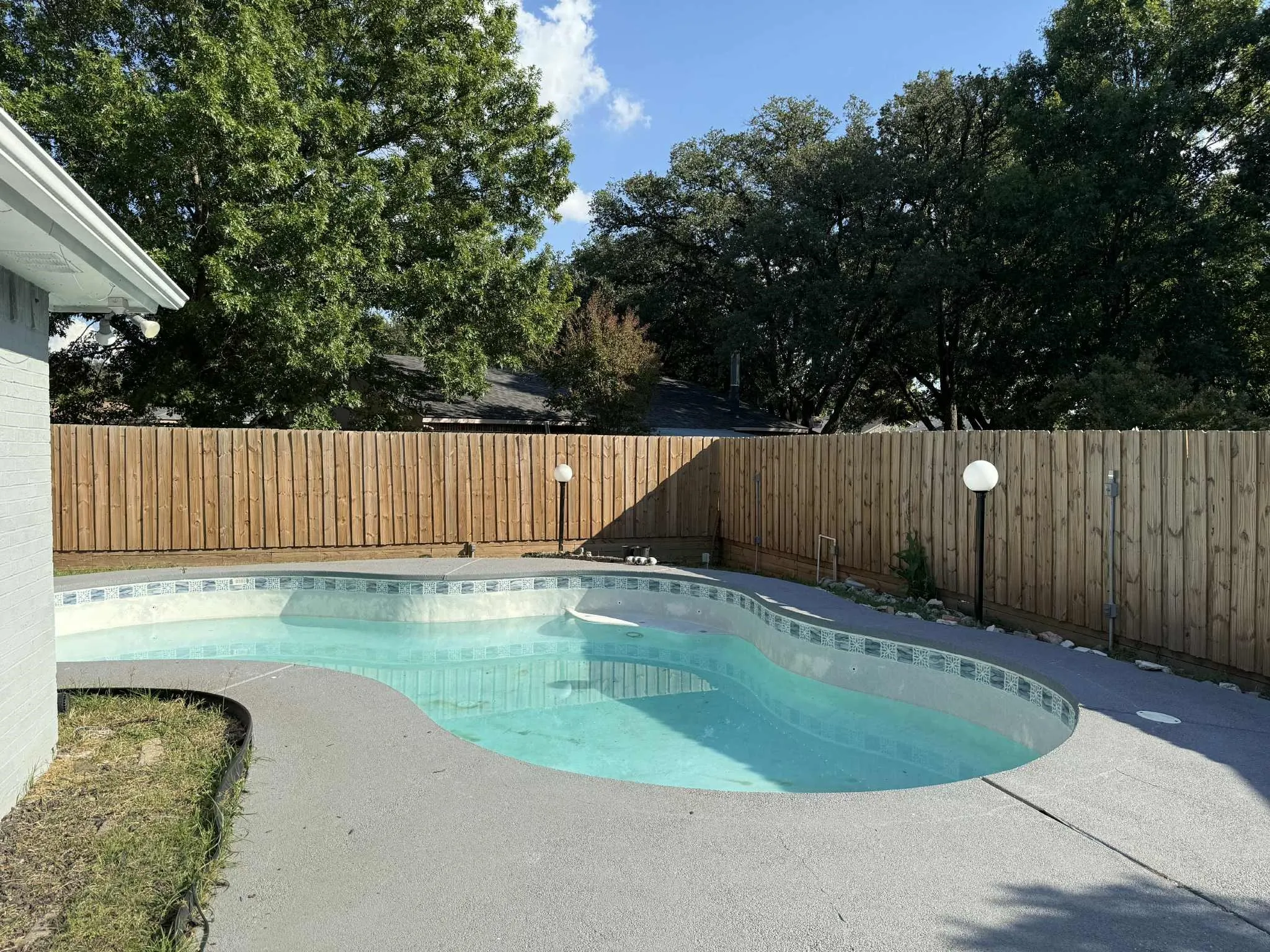 Freeform swimming pool featuring a tiled waterline, concrete decking, and a wood privacy fence