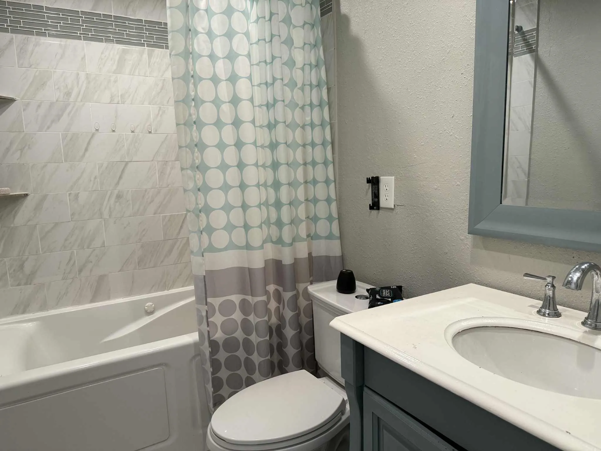 Bathroom featuring a bathtub with subway tile surround, integrated shelving, a white vanity with an integrated sink, and a framed mirror